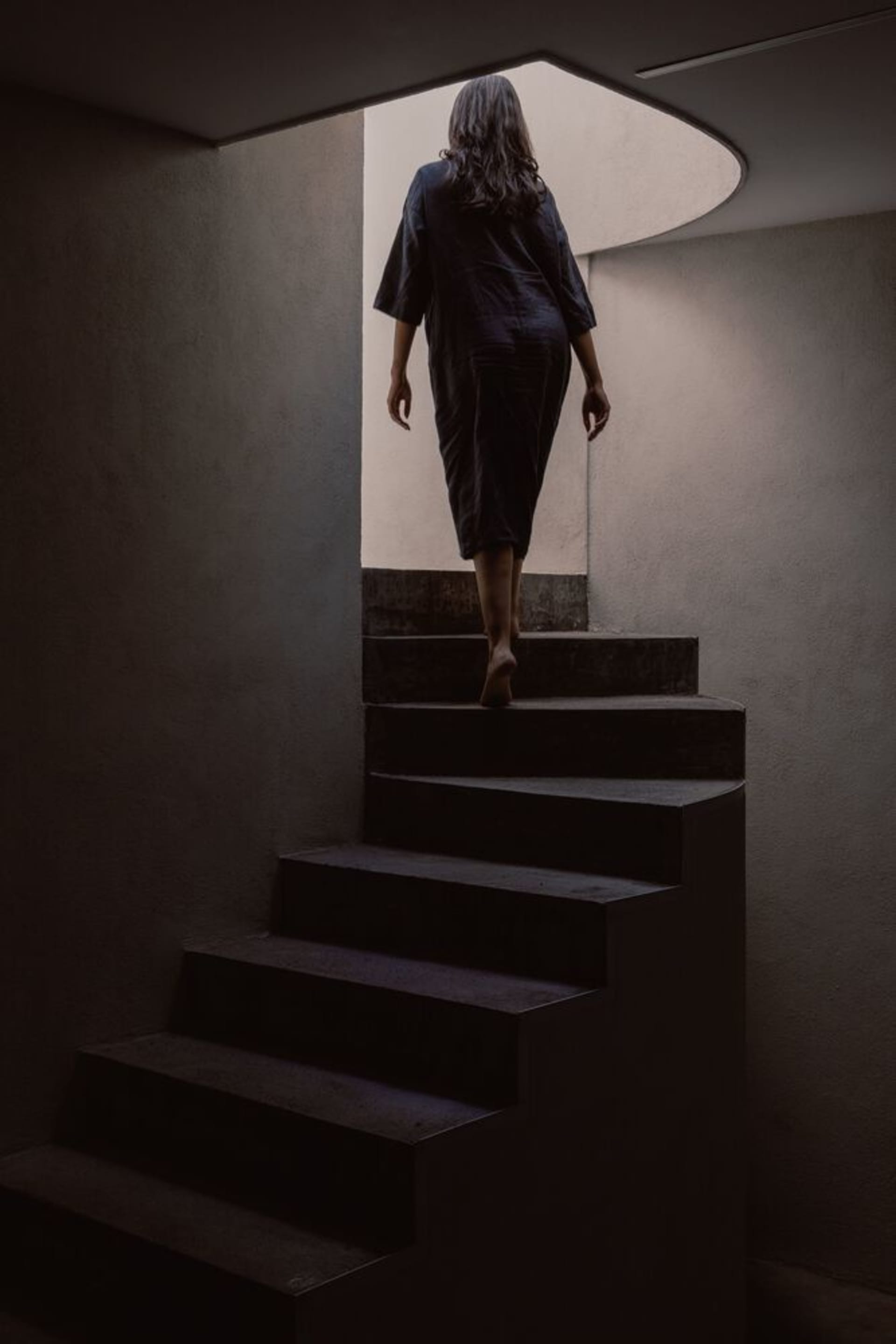 A woman walking up a set of minimalist concrete stairs, viewed from the rear.