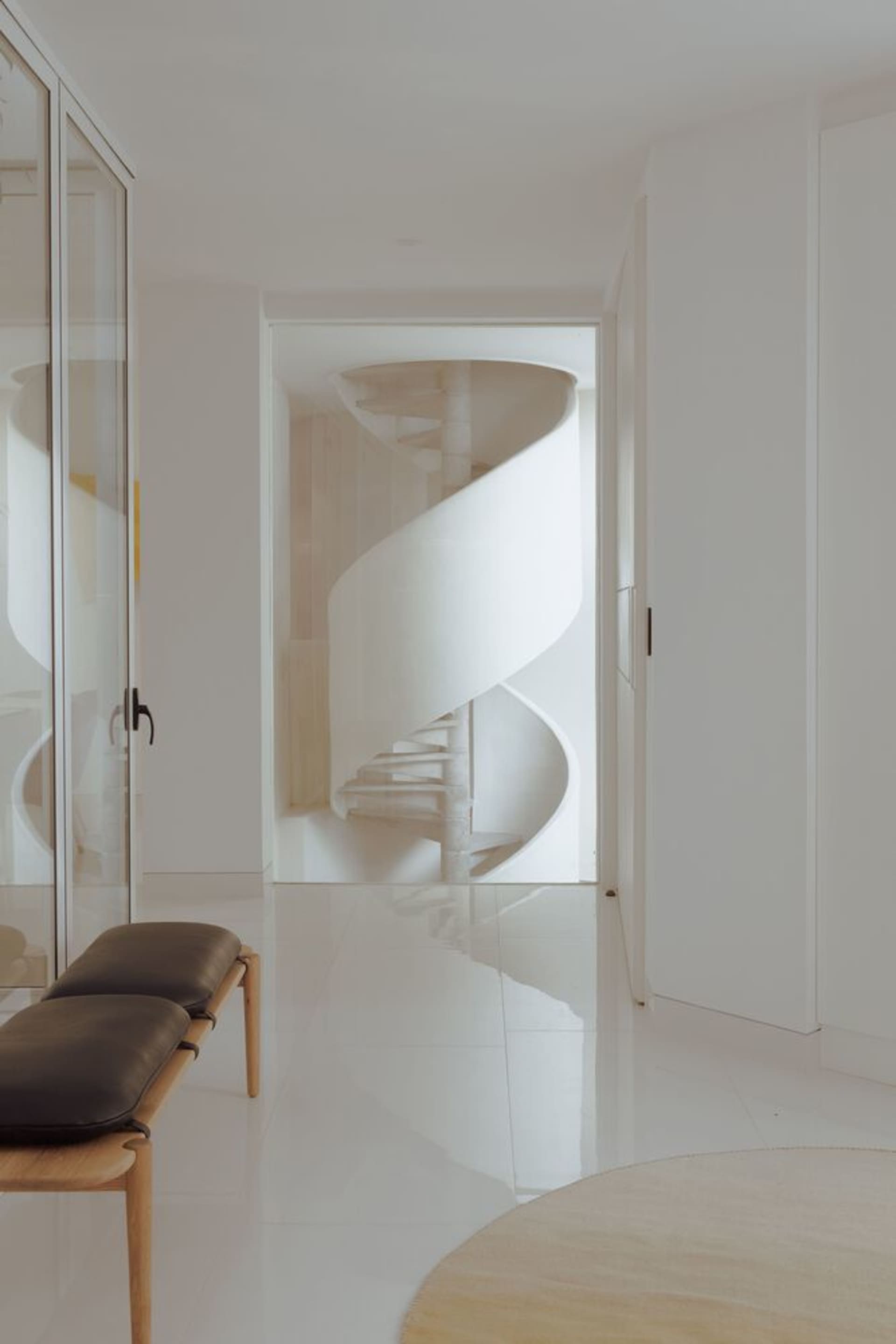 Modern spiral staircase with white marble steps surrounded by glass railings and walls.