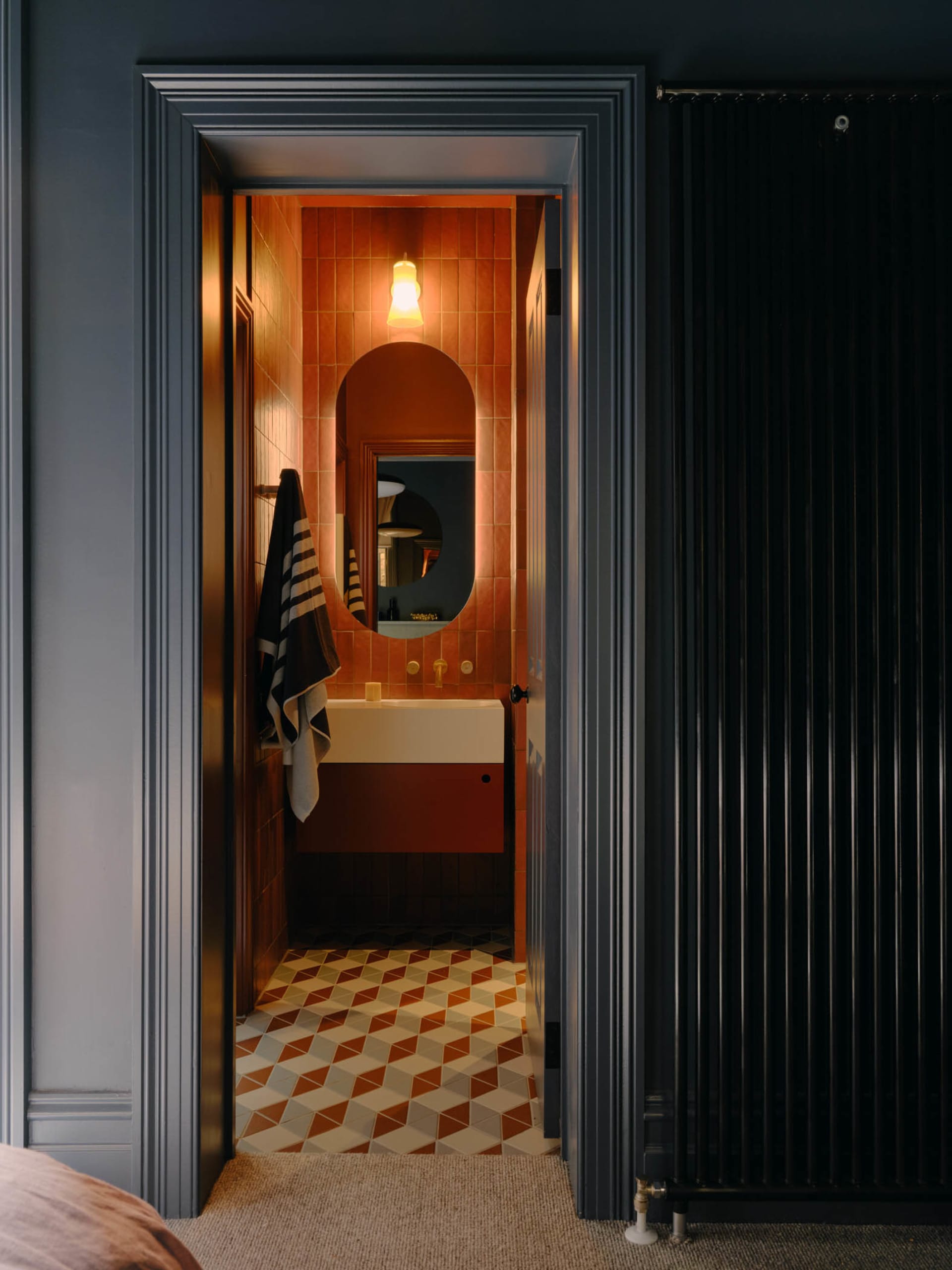 A modern bathroom with orange ceramic tiles, a floating sink, and a round mirror.