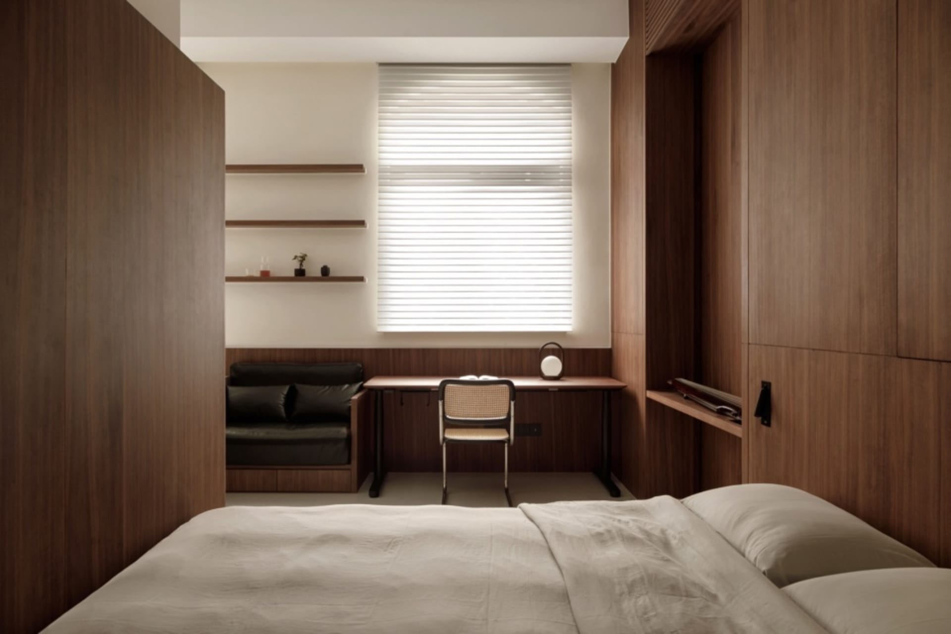 A modern minimalist bedroom with wooden walls, a bed, a desk, and a window with blinds.