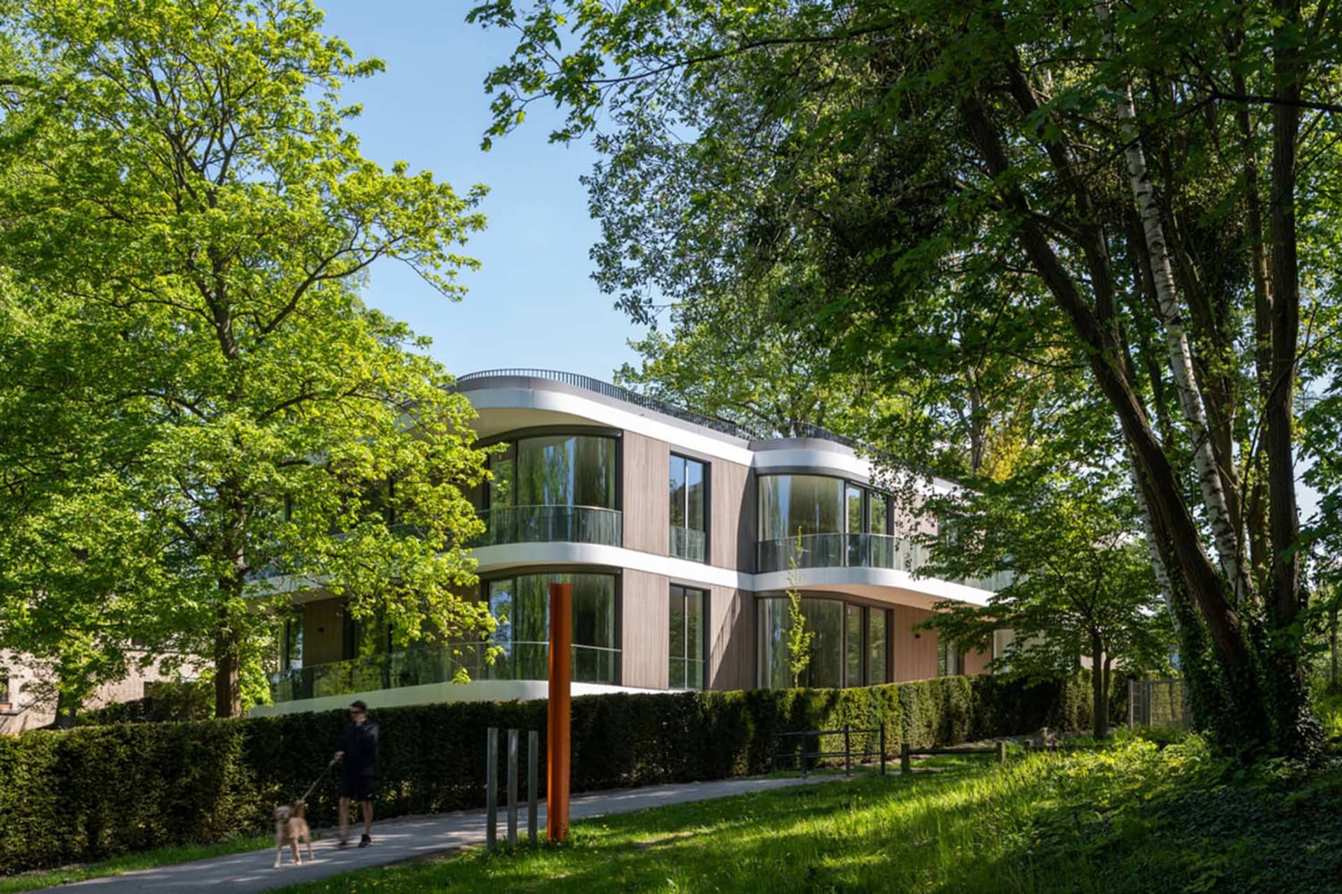 Modern residential construction featuring wood and glass materials and green landscaping.