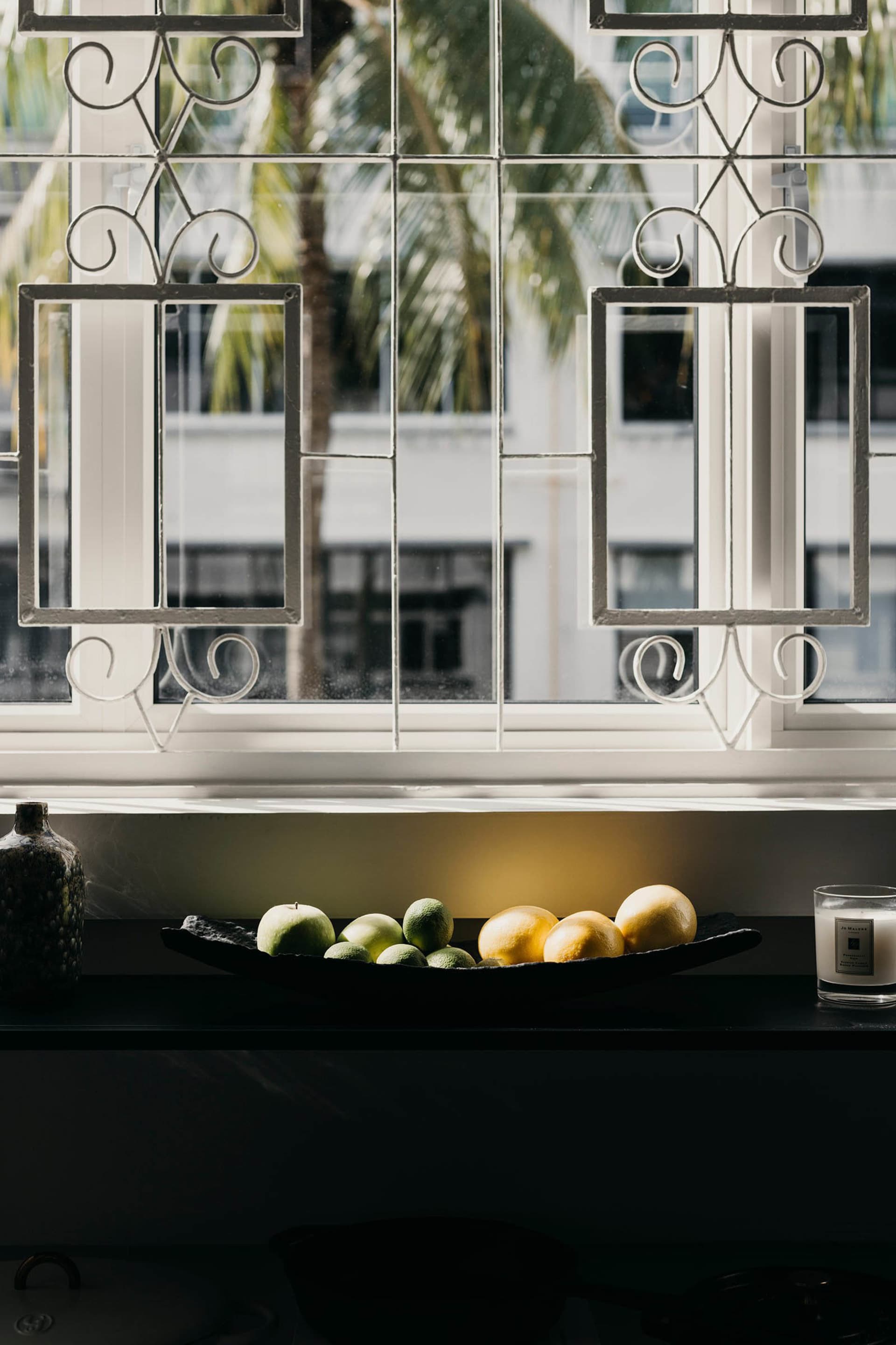 A modern kitchen counter with a white marble top, featuring a bowl of assorted green and yellow fruits.