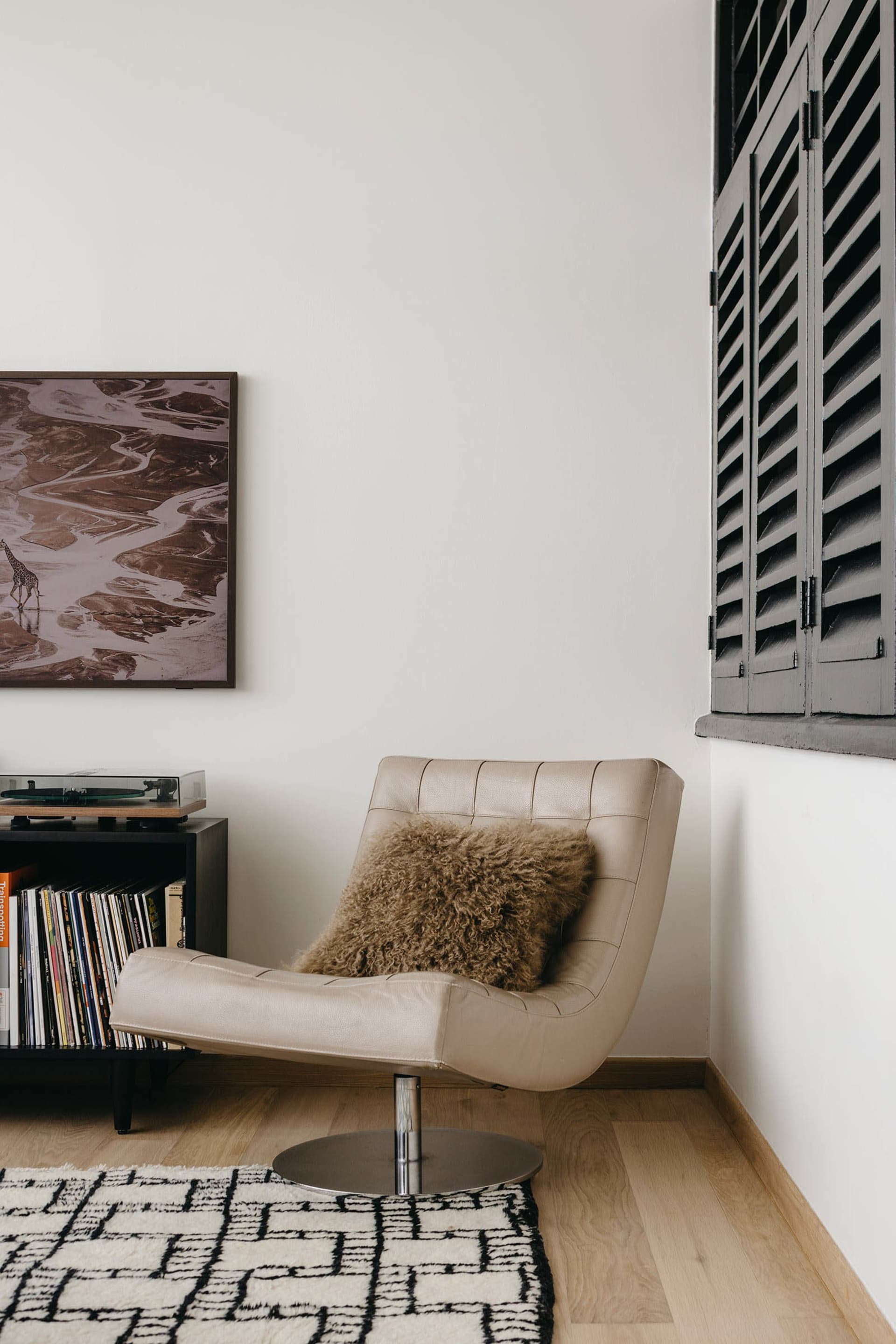A modern leather chair with a fluffy pillow in a room with white walls and a wooden floor.