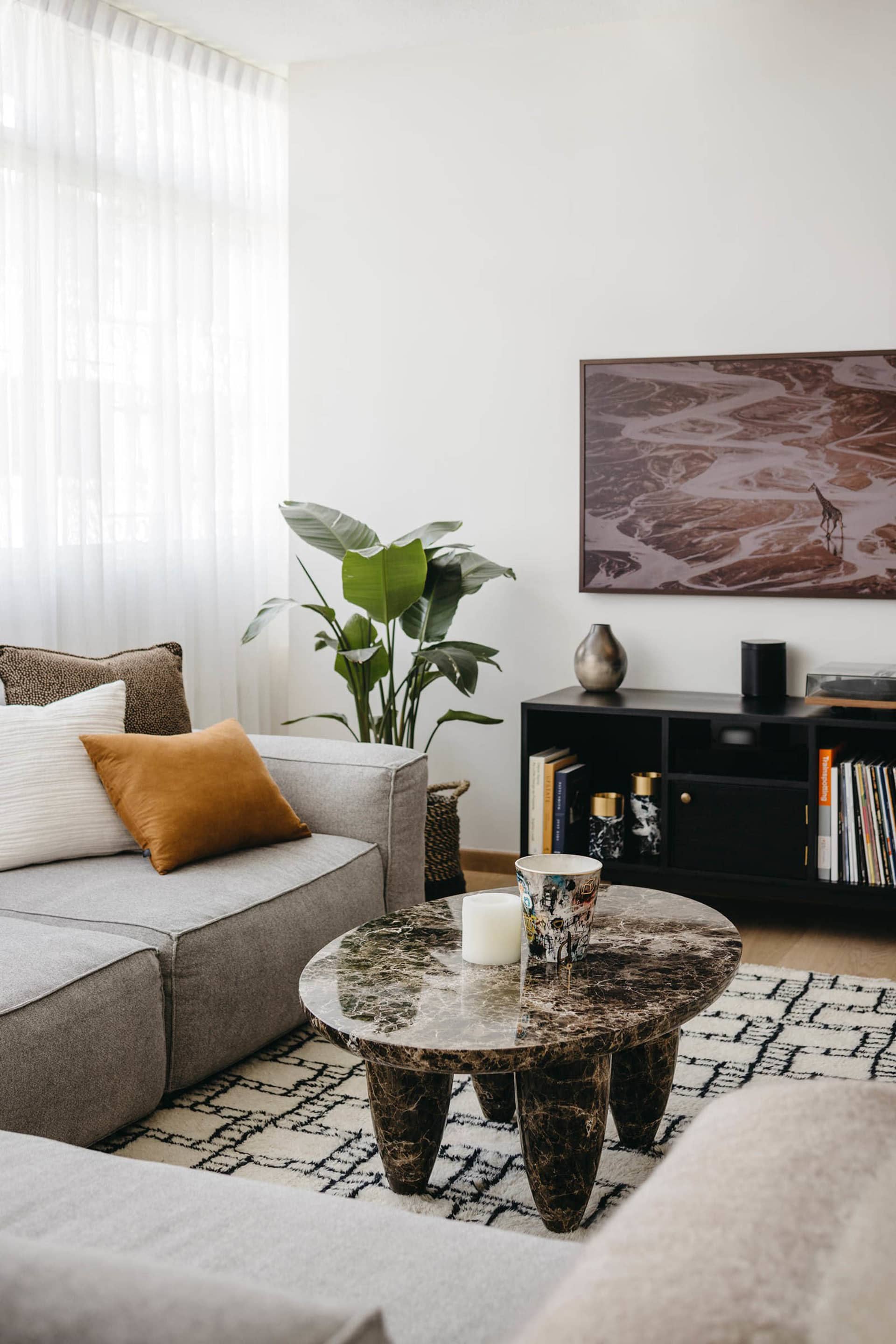 A modern living room with a gray sectional sofa adorned with decorative pillows, a round marble coffee table, and a dark book