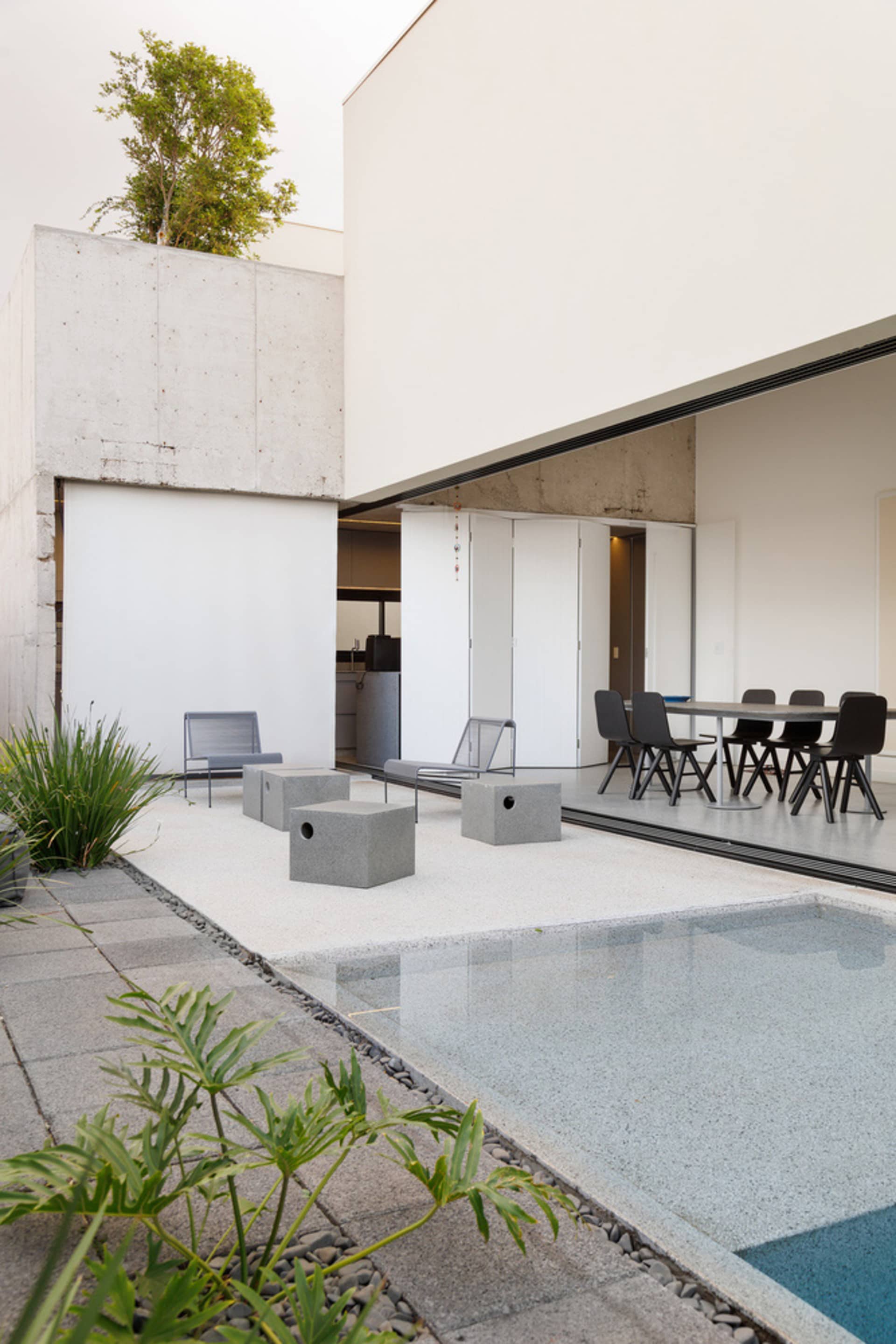 A minimalist patio with concrete furniture and a swimming pool, with a modern building in the background.