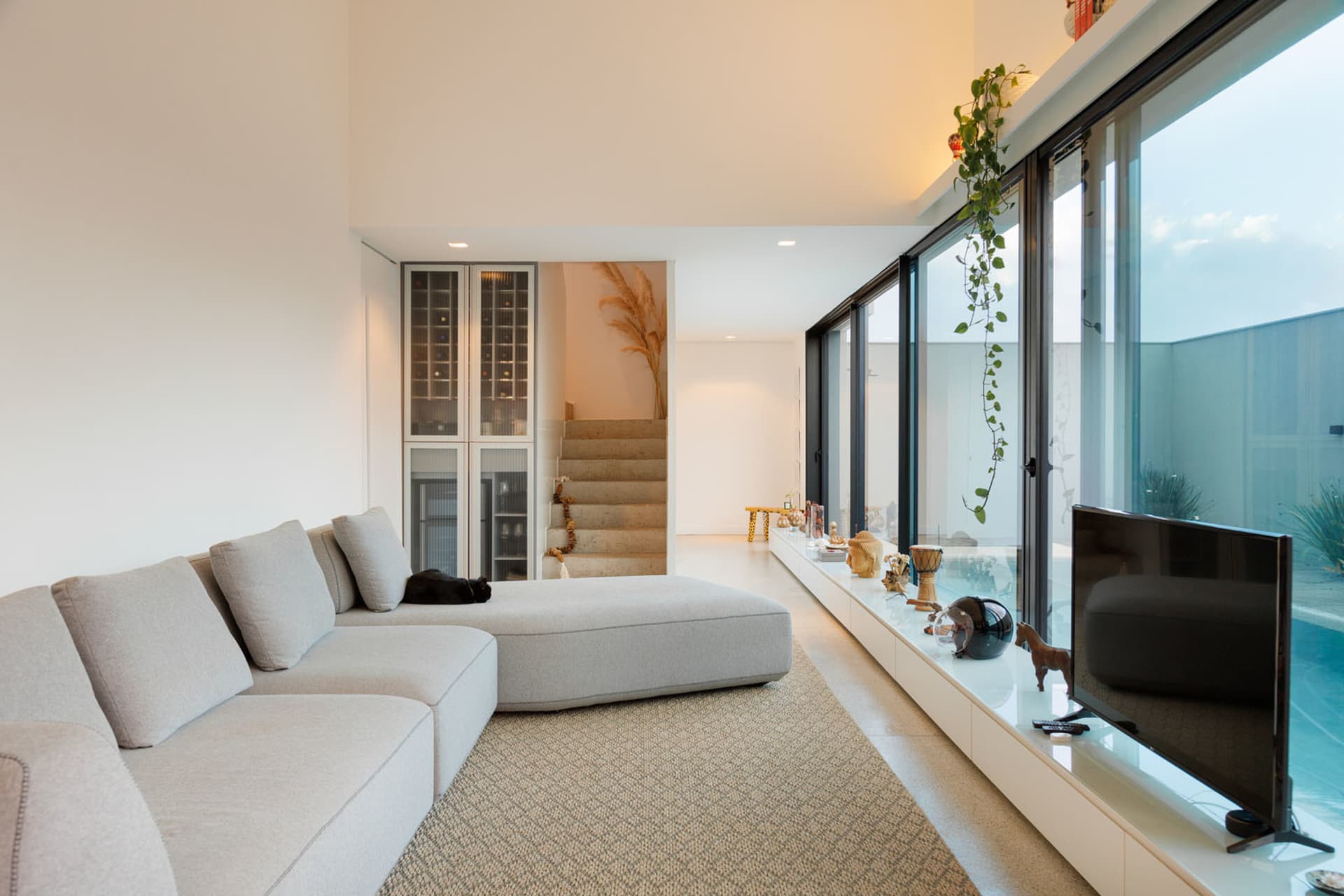 A modern minimalist living room with concrete walls and floor, featuring a sleek white couch and a television on a glass shel
