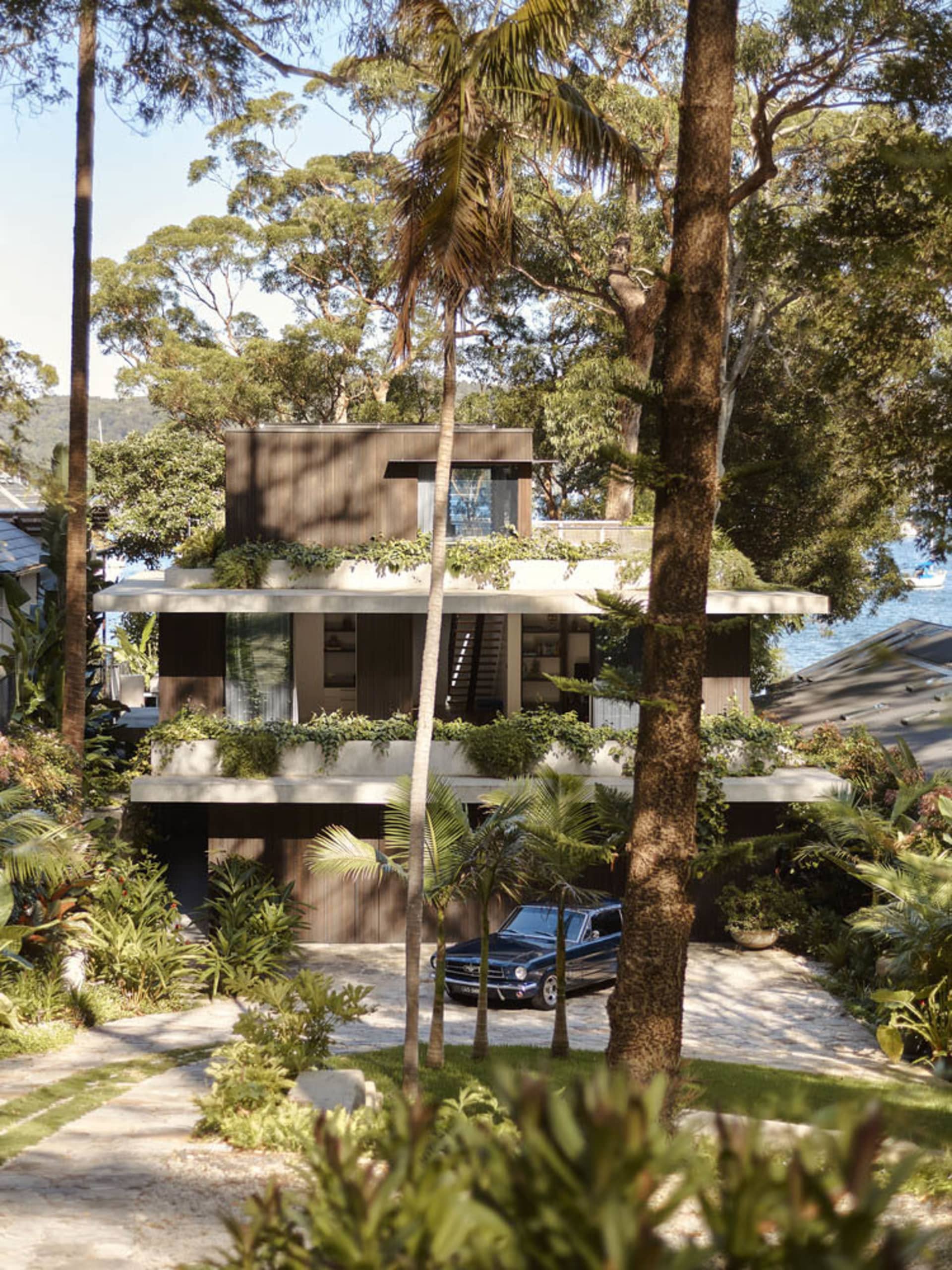 一座擁有屋頂花園的現代住宅,周圍環繞樹木與綠意,車道上停放著一輛藍色汽車。