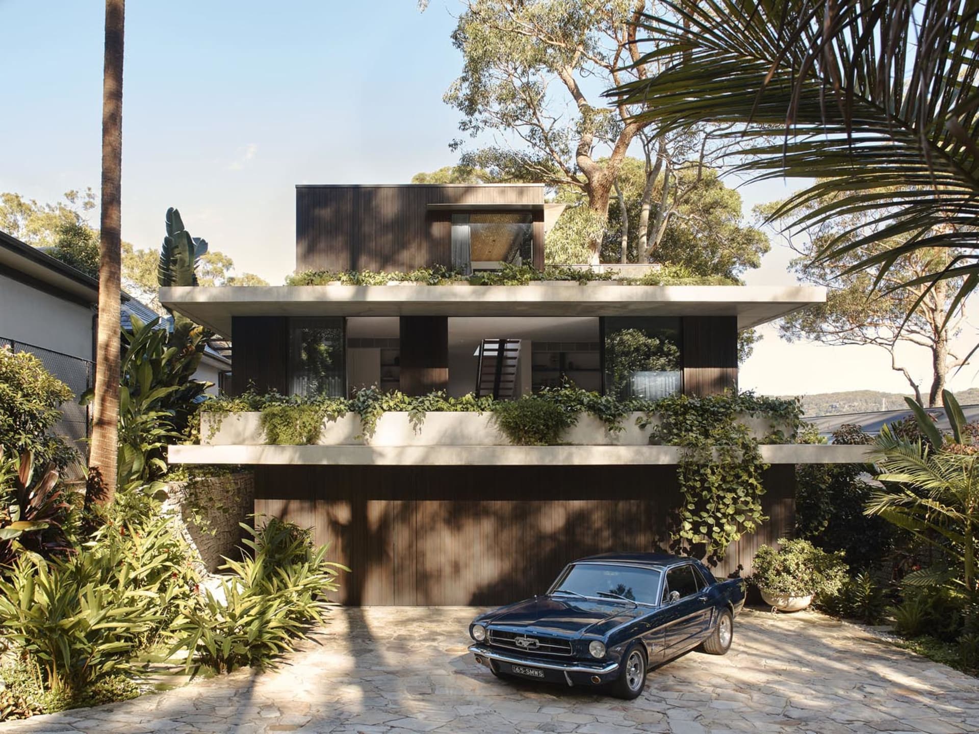 Modern house with concrete exterior, green plants, and a vintage car parked in front.