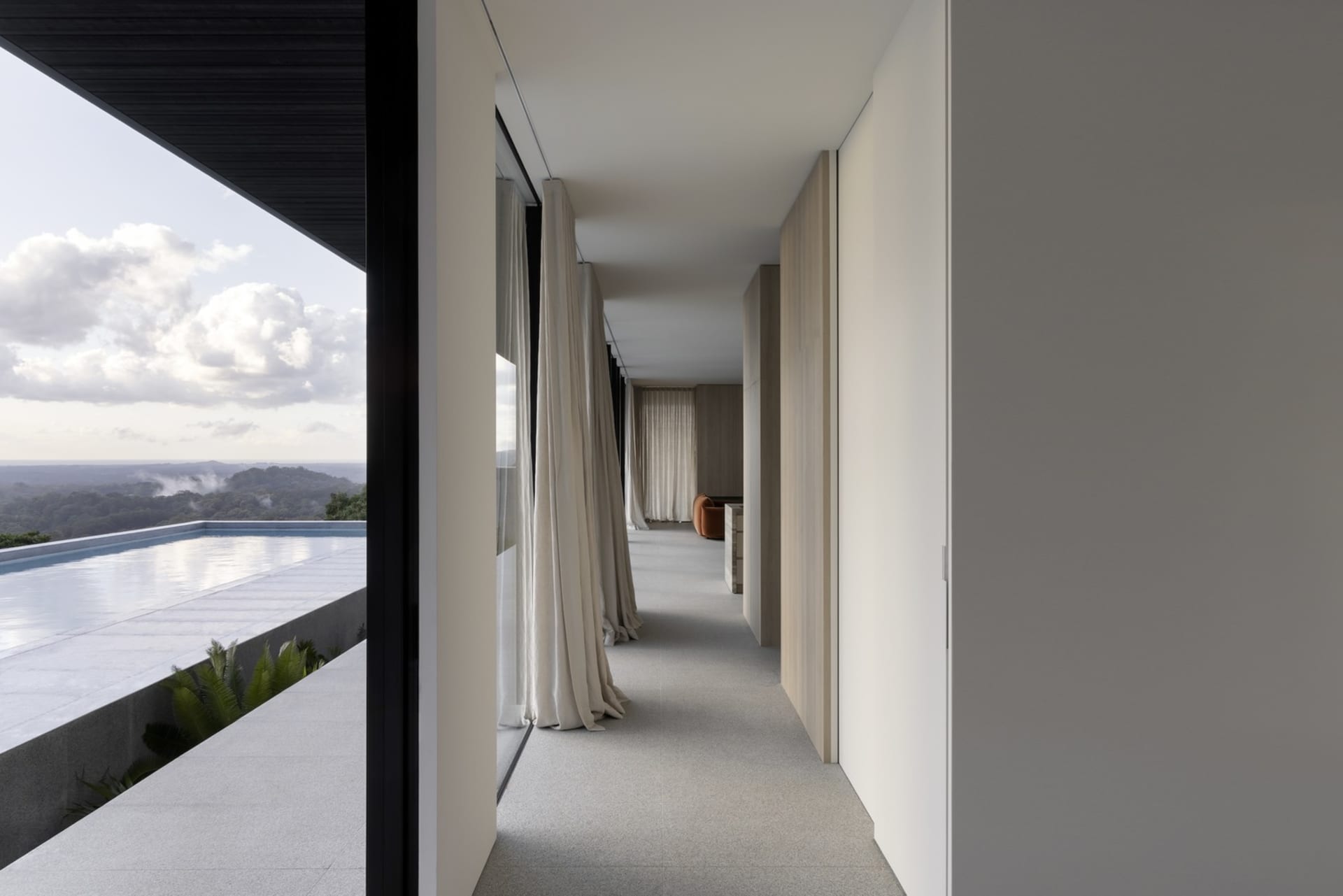 Modern, minimalist corridor with concrete walls, white curtains, and a view of clouds and mountains.