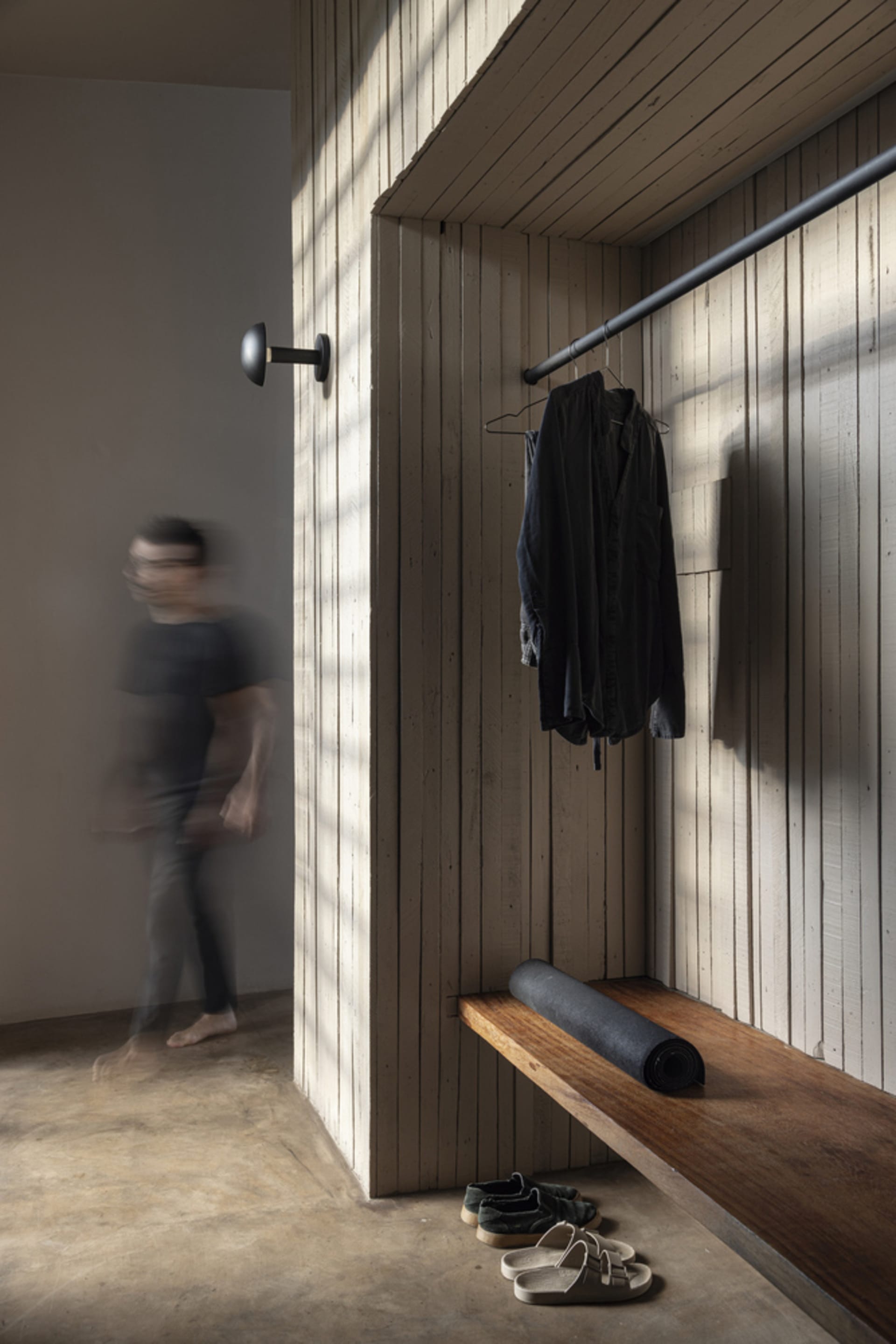 A minimalist entryway featuring a wooden bench, yoga mat, and hanging clothing.