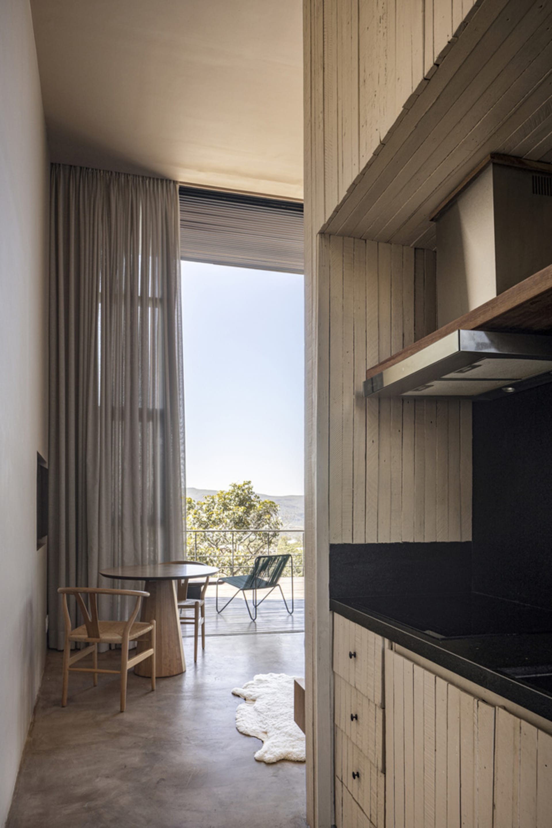 A minimalist residential kitchen featuring wood elements and a view of the outdoors through sheer curtains.