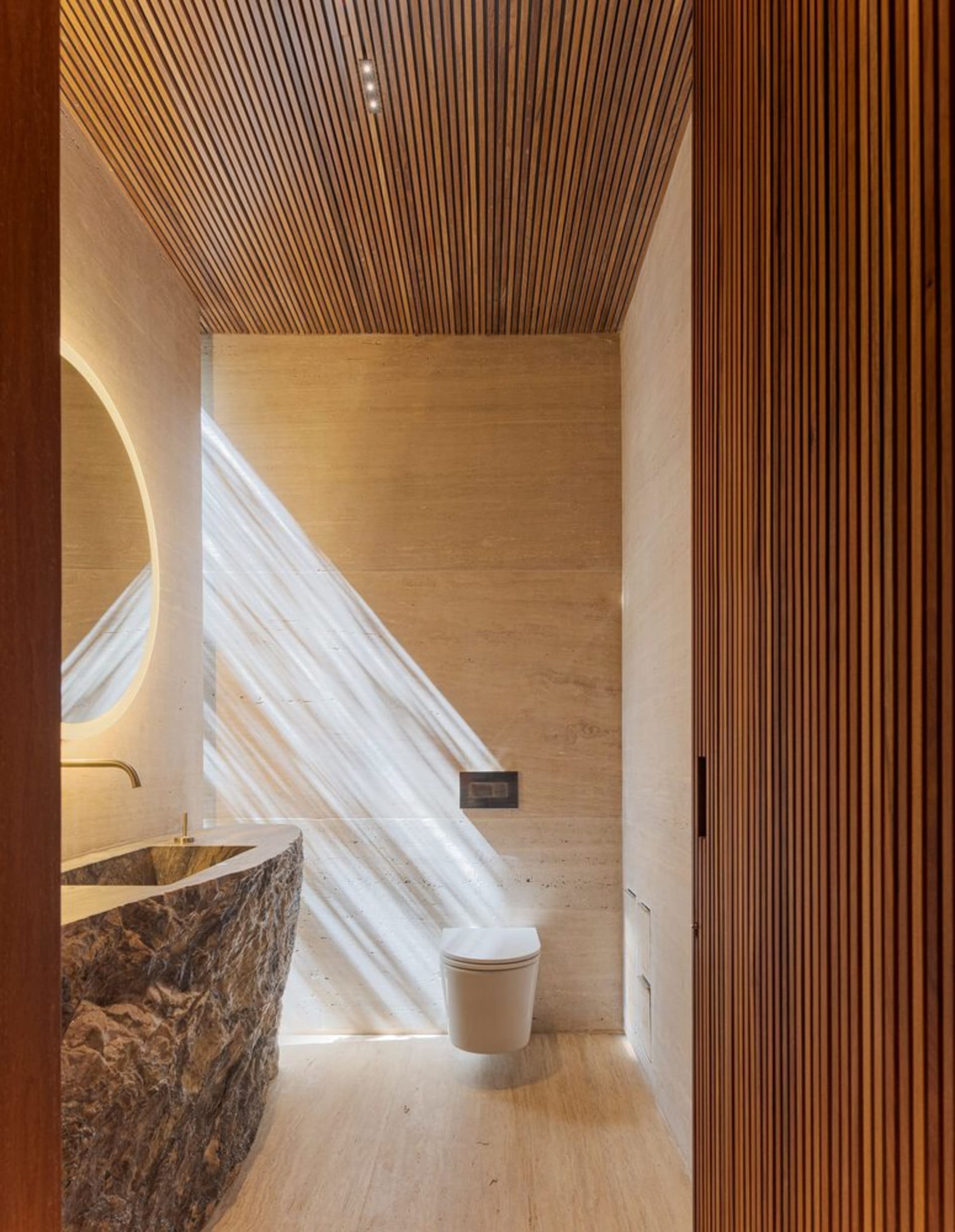 Modern bathroom featuring a stone tile floor and walls, sleek fixtures, and a wooden door with vertical slats.