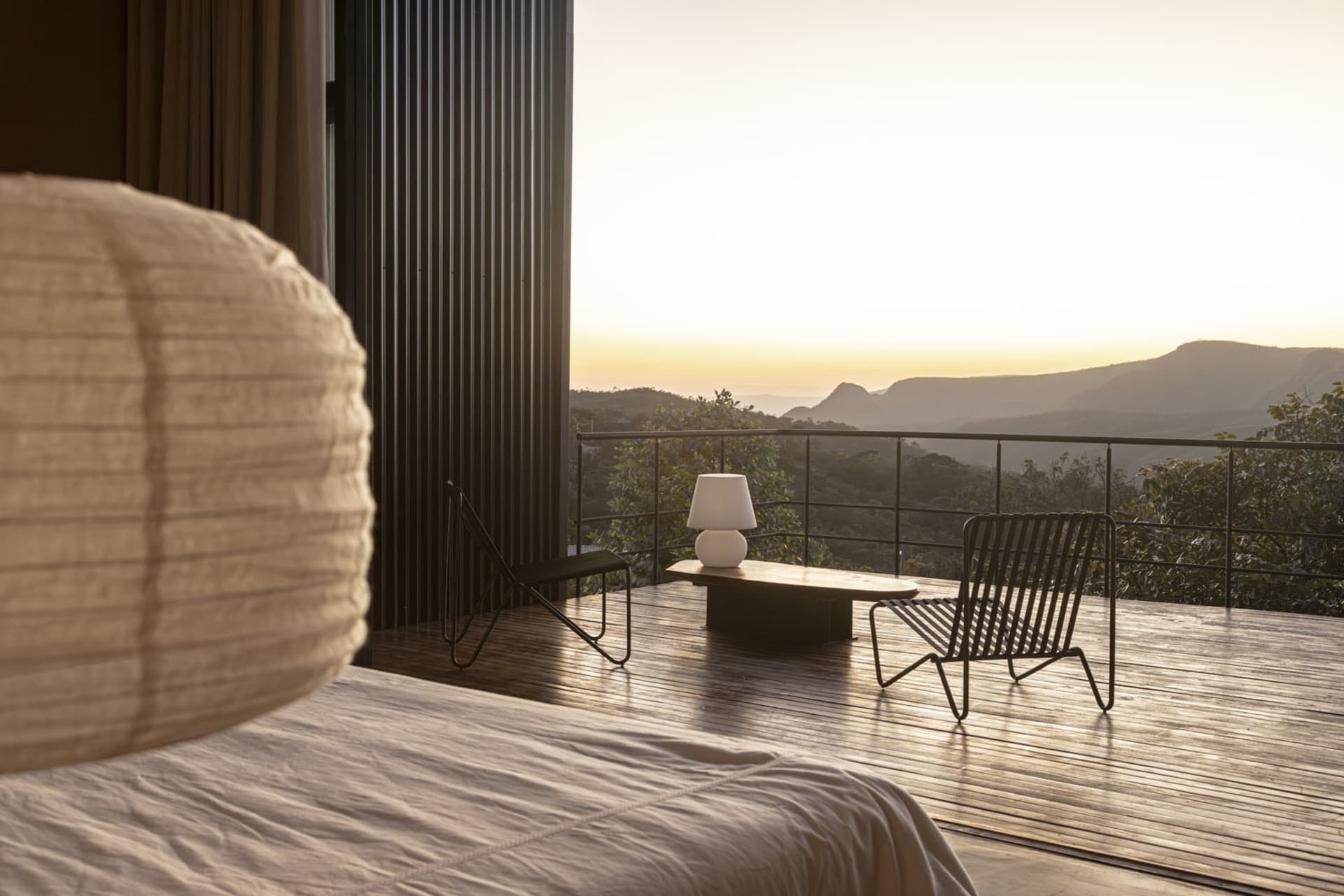 A modern bedroom featuring a wooden floor with a large window overlooking mountains at sunset.