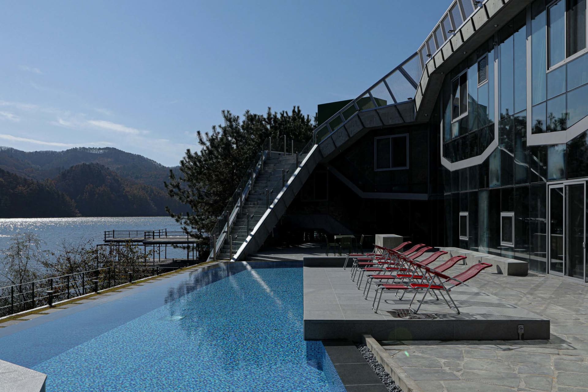 現代玻璃與金屬外觀的湖畔住宅,俯瞰湖景,並設有戶外泳池與紅色休閒椅。