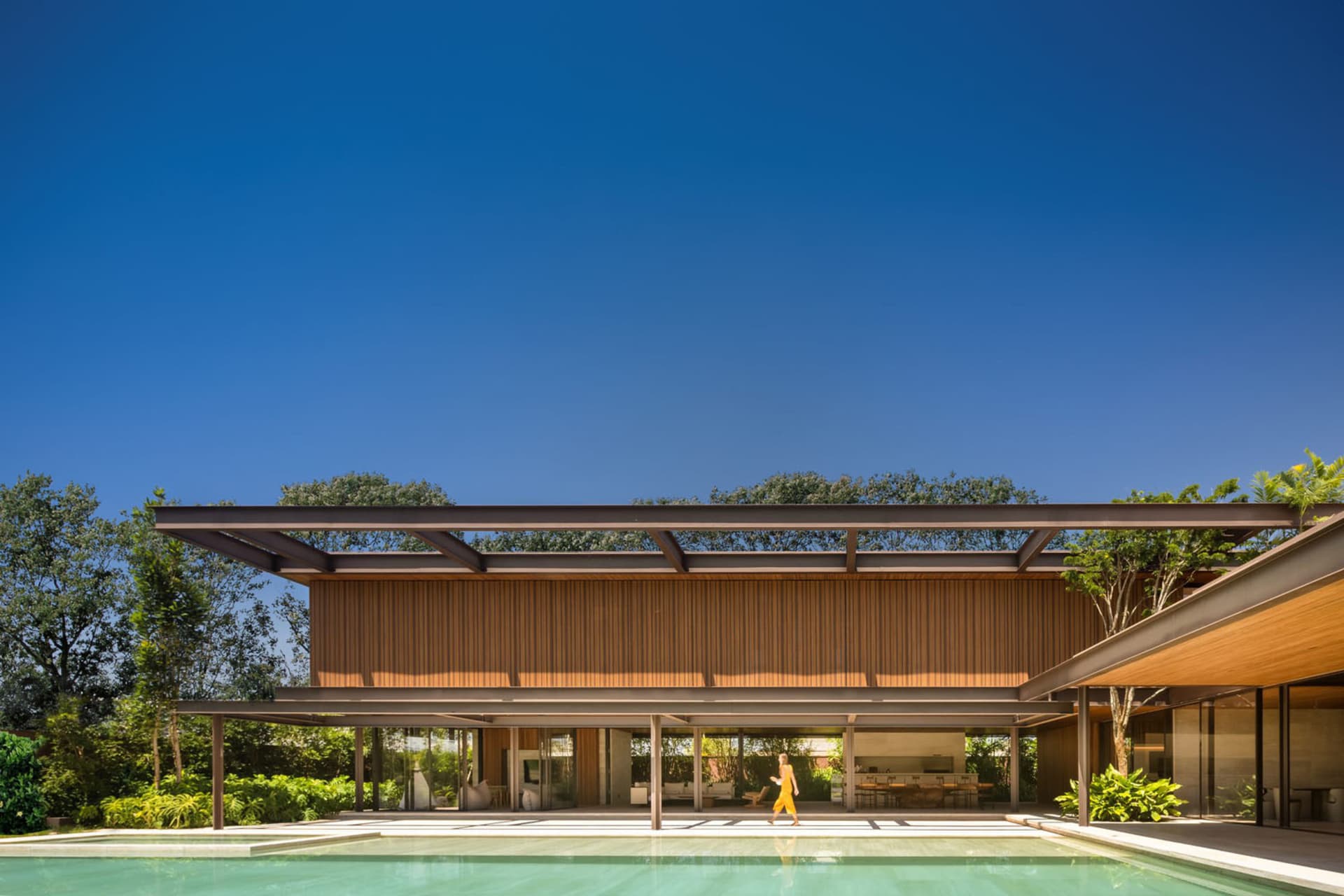 Modern residential exterior with a pool, featuring wood, glass, concrete, and metal materials.
