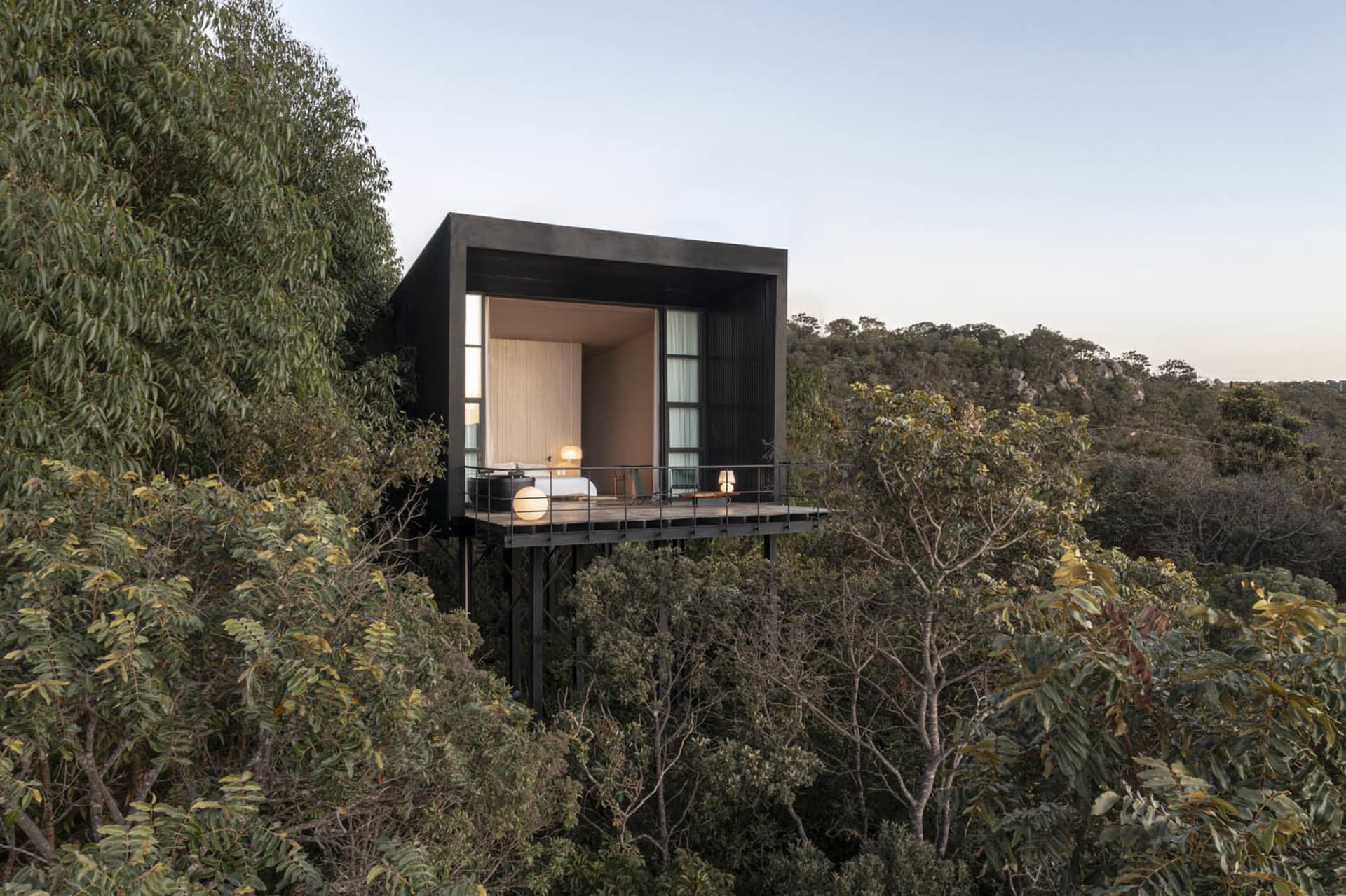 Minimalist, modern treehouse residence with black exterior and white interiors, elevated on stilts over dense forest.