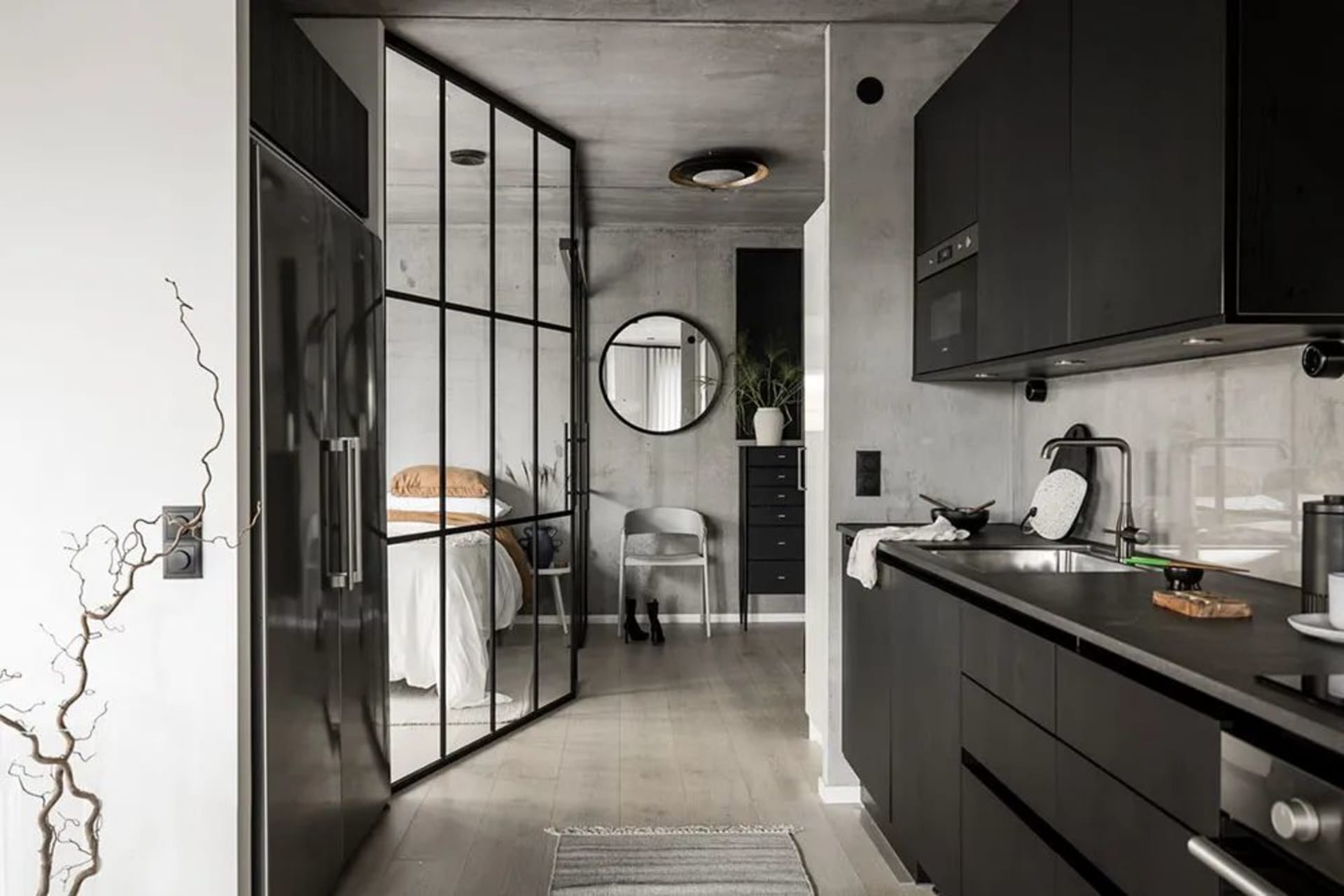 Industrial-inspired black kitchen with concrete panel walls, framed glass walls connecting to bedroom, and black steel kitche