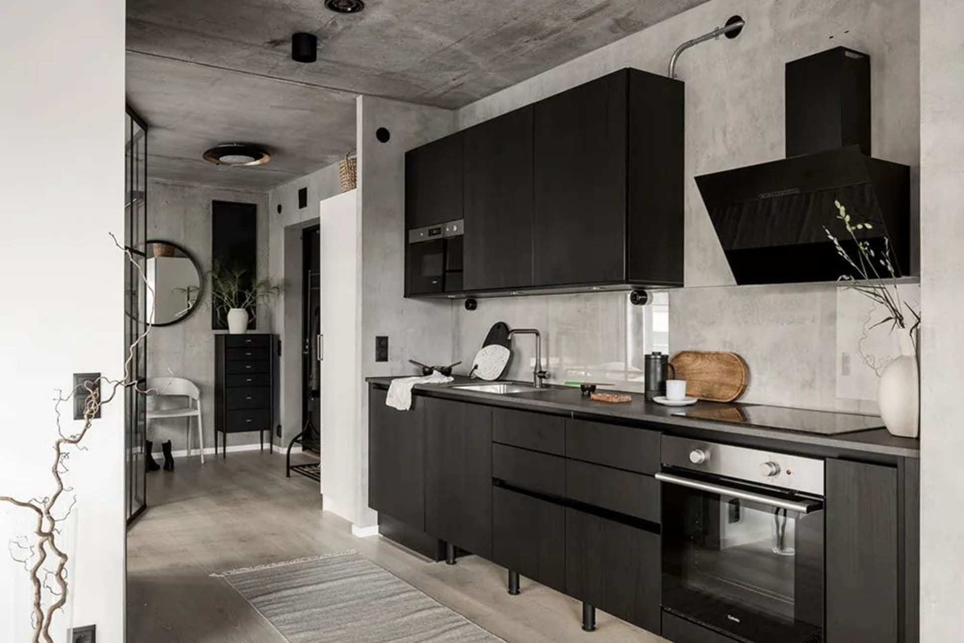 A contemporary kitchen with black cabinets, concrete walls, and wood accents, featuring a modern kitchen sink, open floor pla
