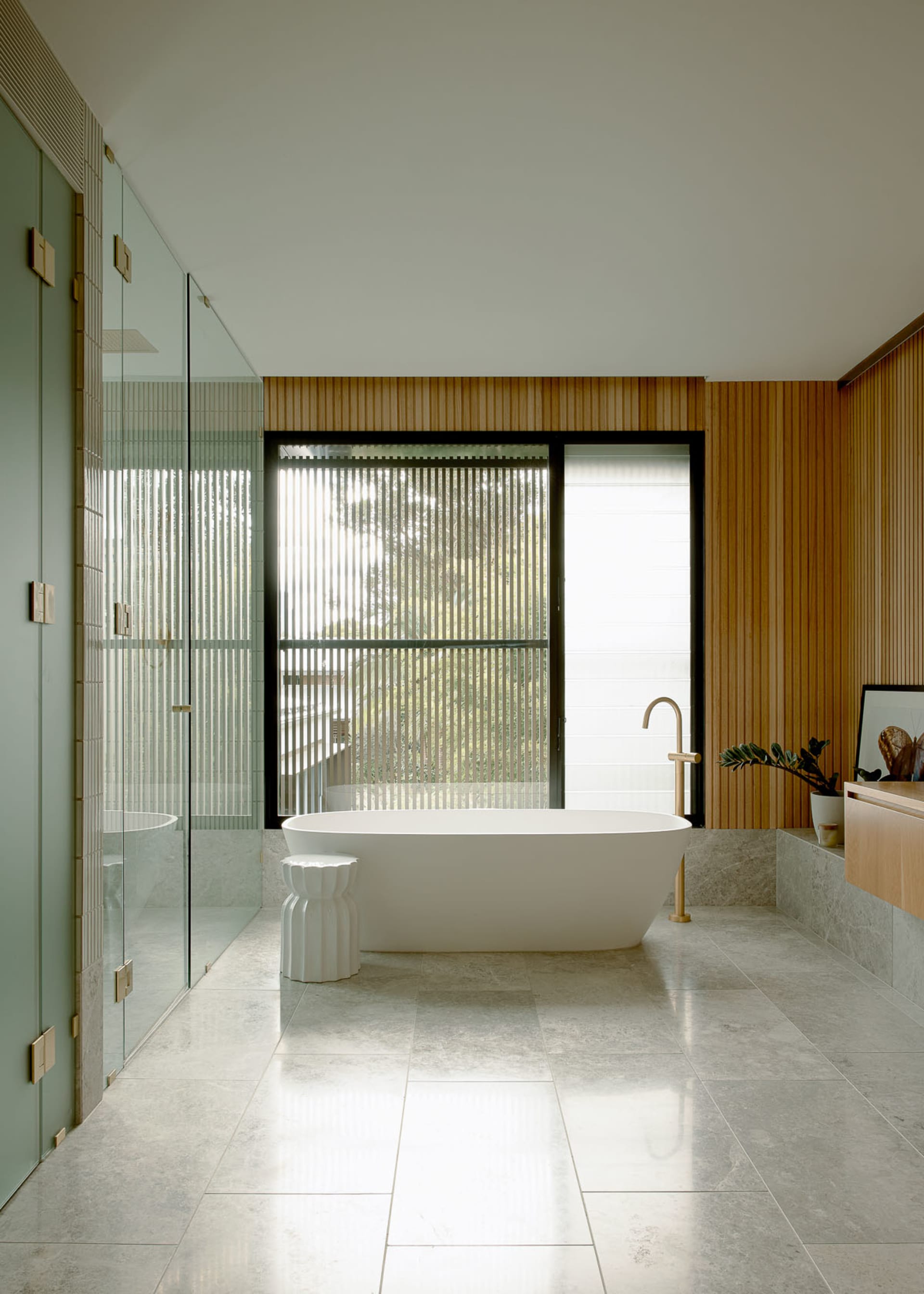 A modern bathroom with concrete flooring, a freestanding bathtub, a wooden accent wall, and a frosted glass shower.
