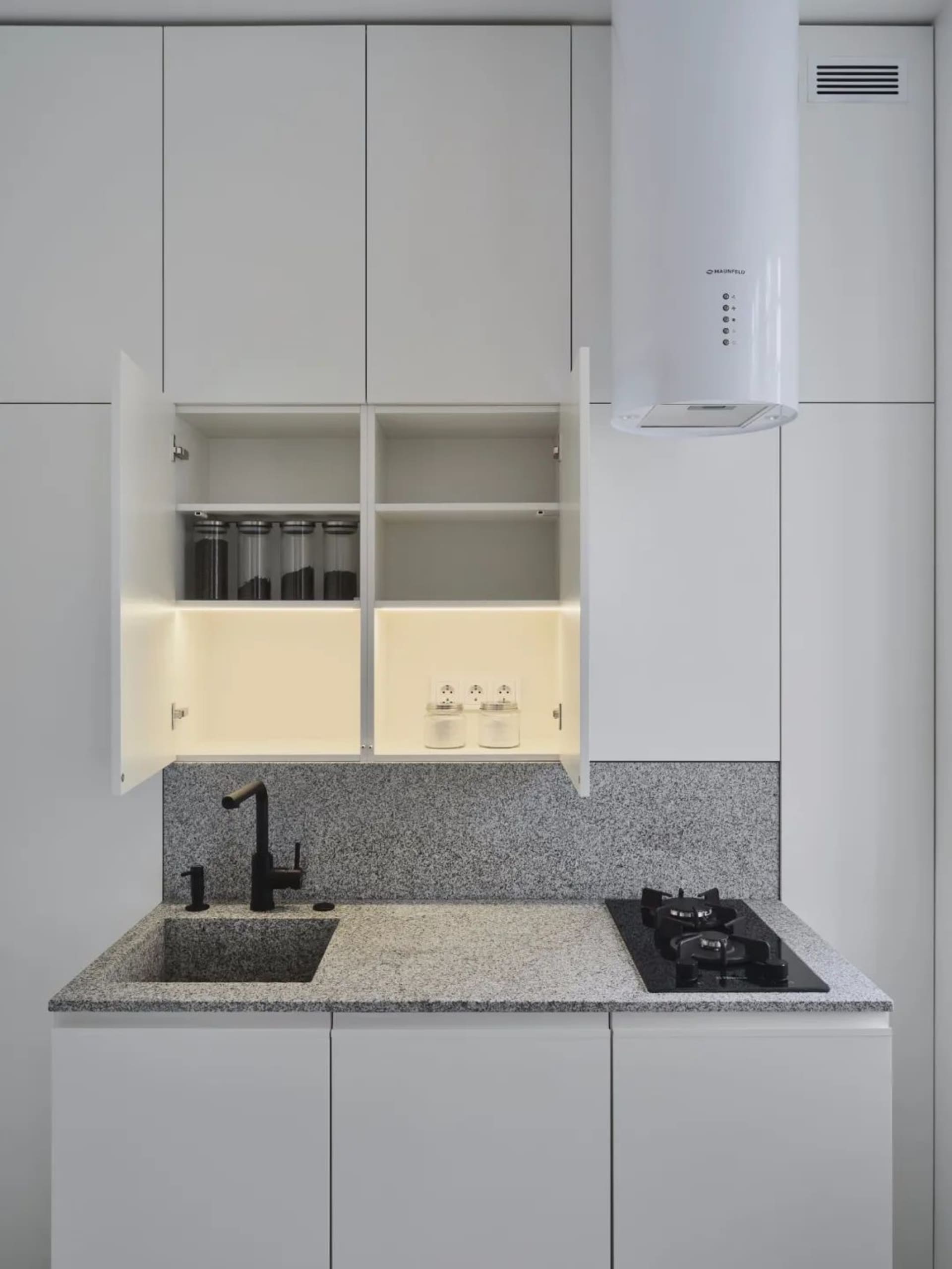 A modern minimalist kitchen with granite countertops and white cabinets.