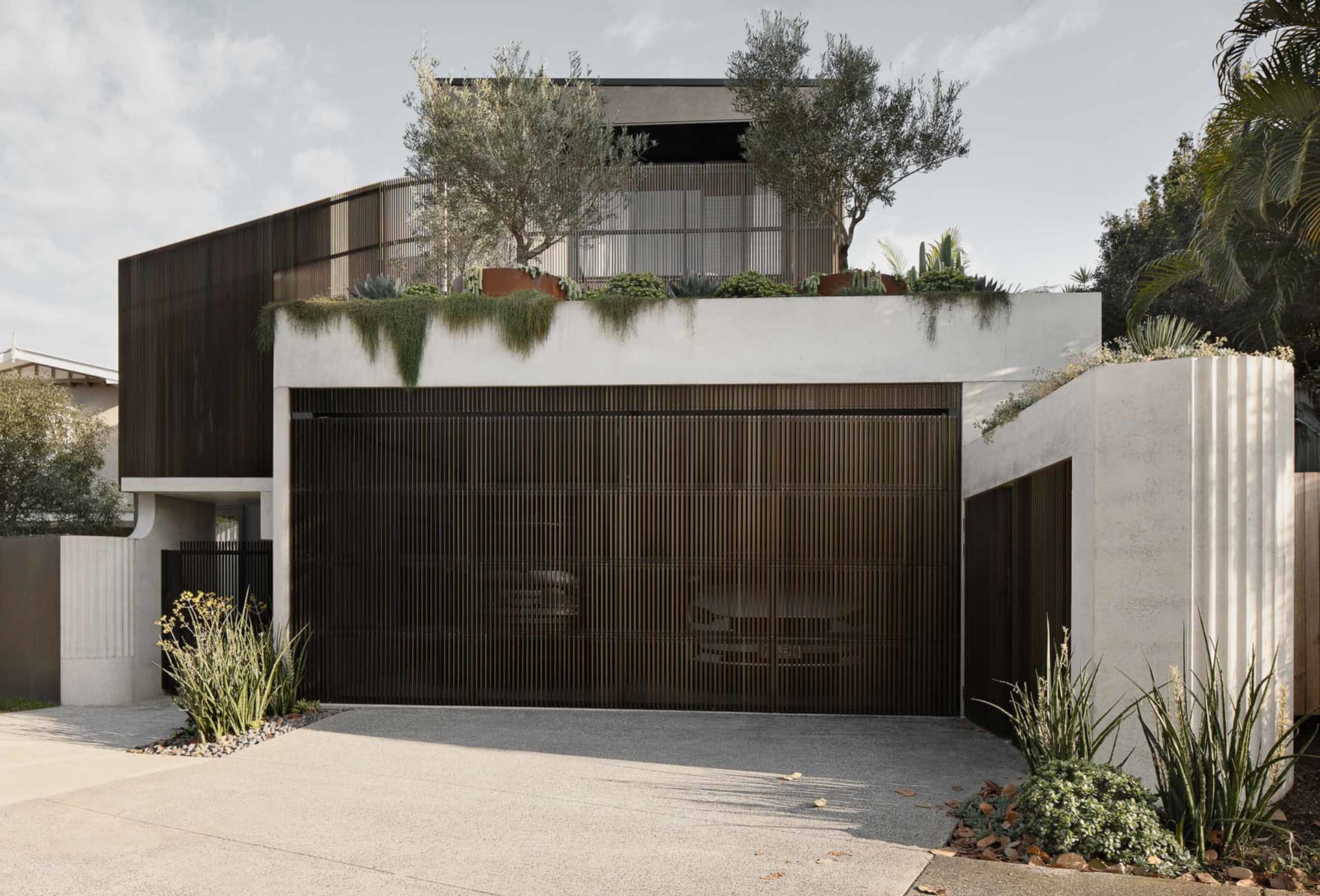 A modern house with metallic door, concrete walls, and greenery on rooftop.