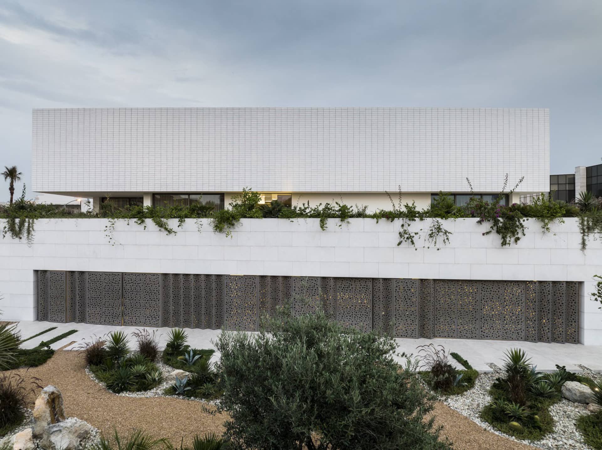 White marble residential building with greenery on the roof and ground floor.