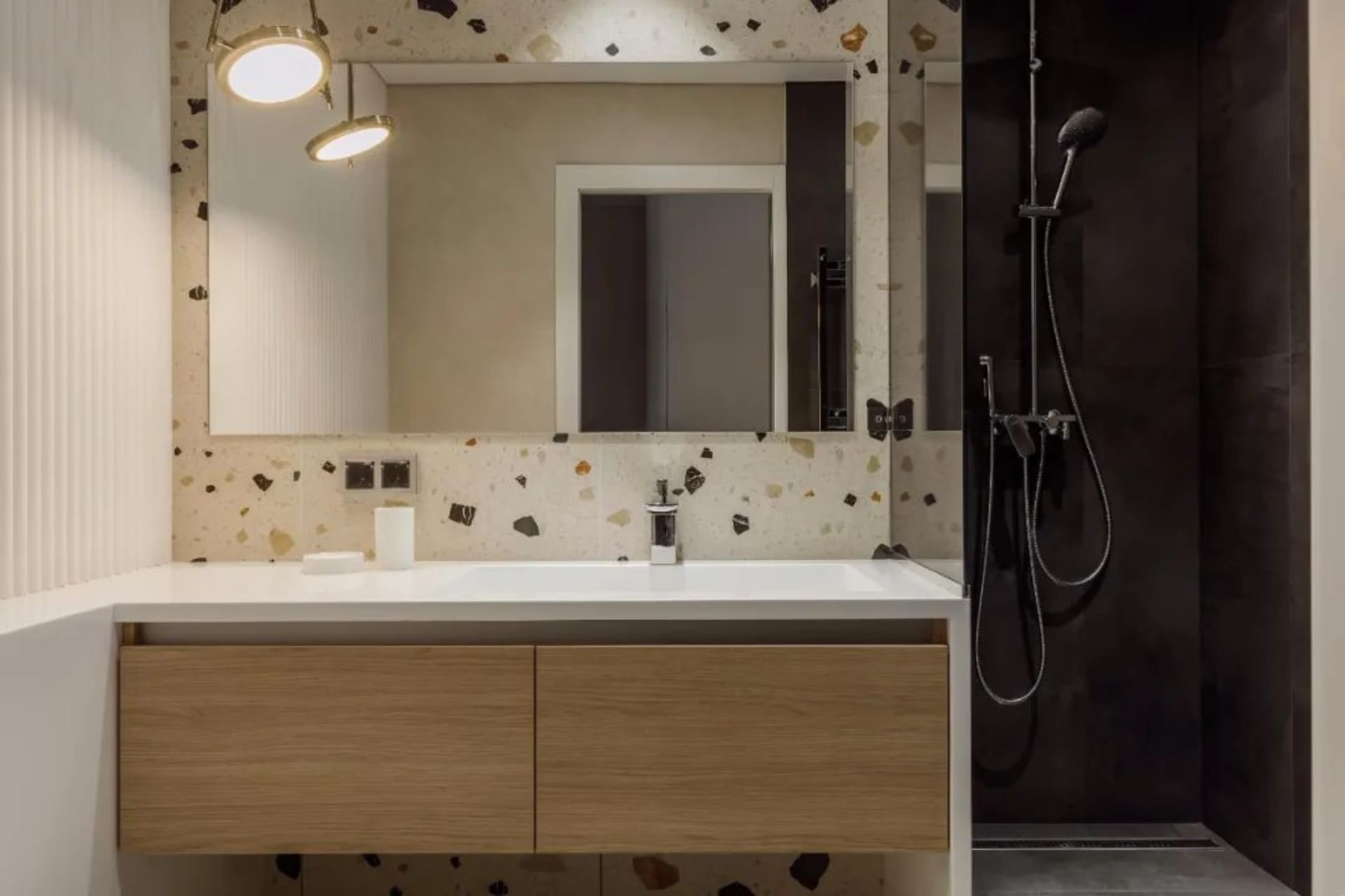 Modern minimalist bathroom with white terrazzo tiles, a floating vanity with wooden drawers, and a glass shower enclosure.