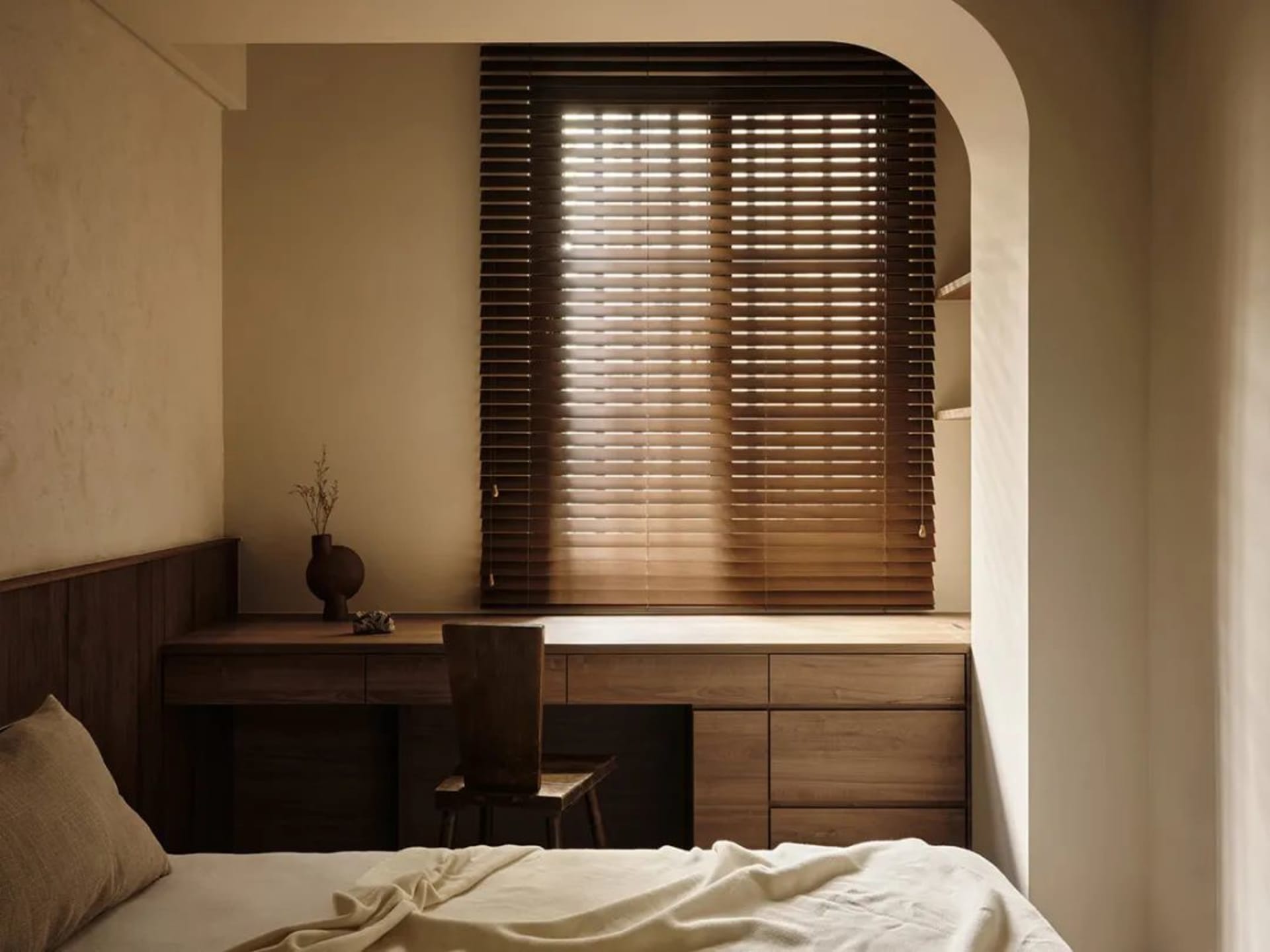 Modern minimalist bedroom featuring wooden blinds and a wooden desk with a chair.