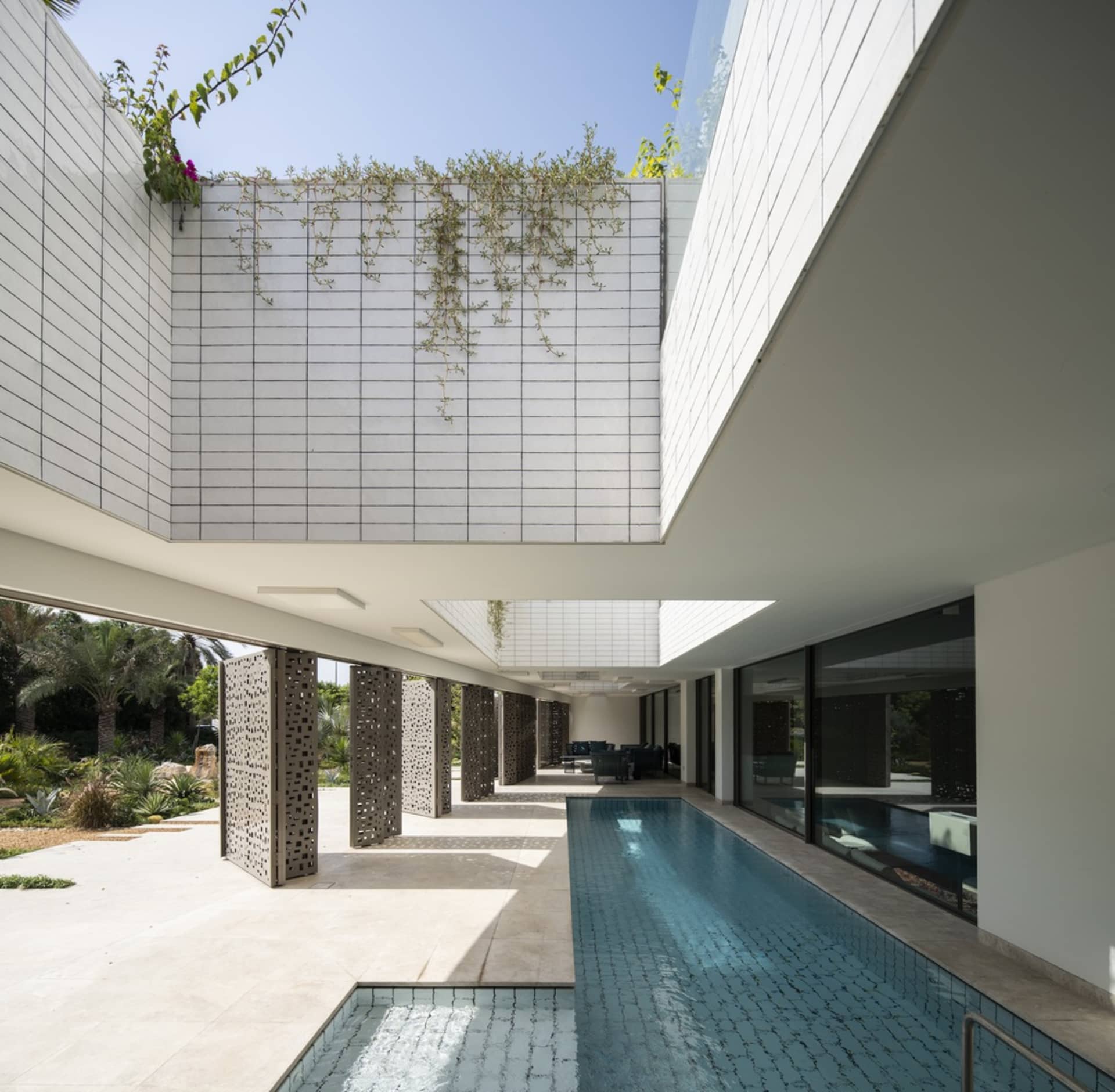 A modern residential house with concrete walls and a pool, featuring plants and a spacious interior.