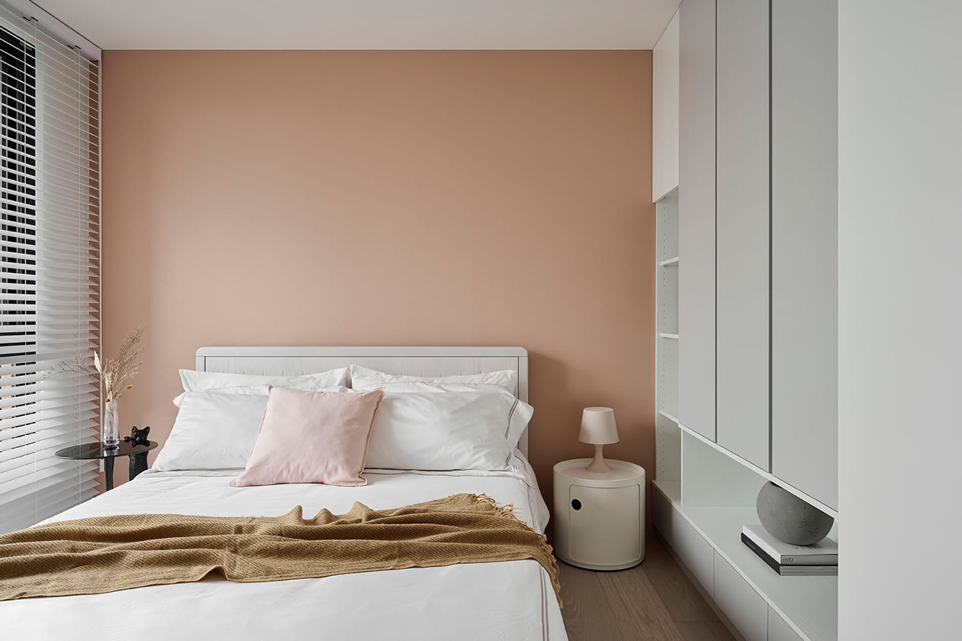 Minimalist bedroom with white furniture, pink accent pillow, and a beige blanket.