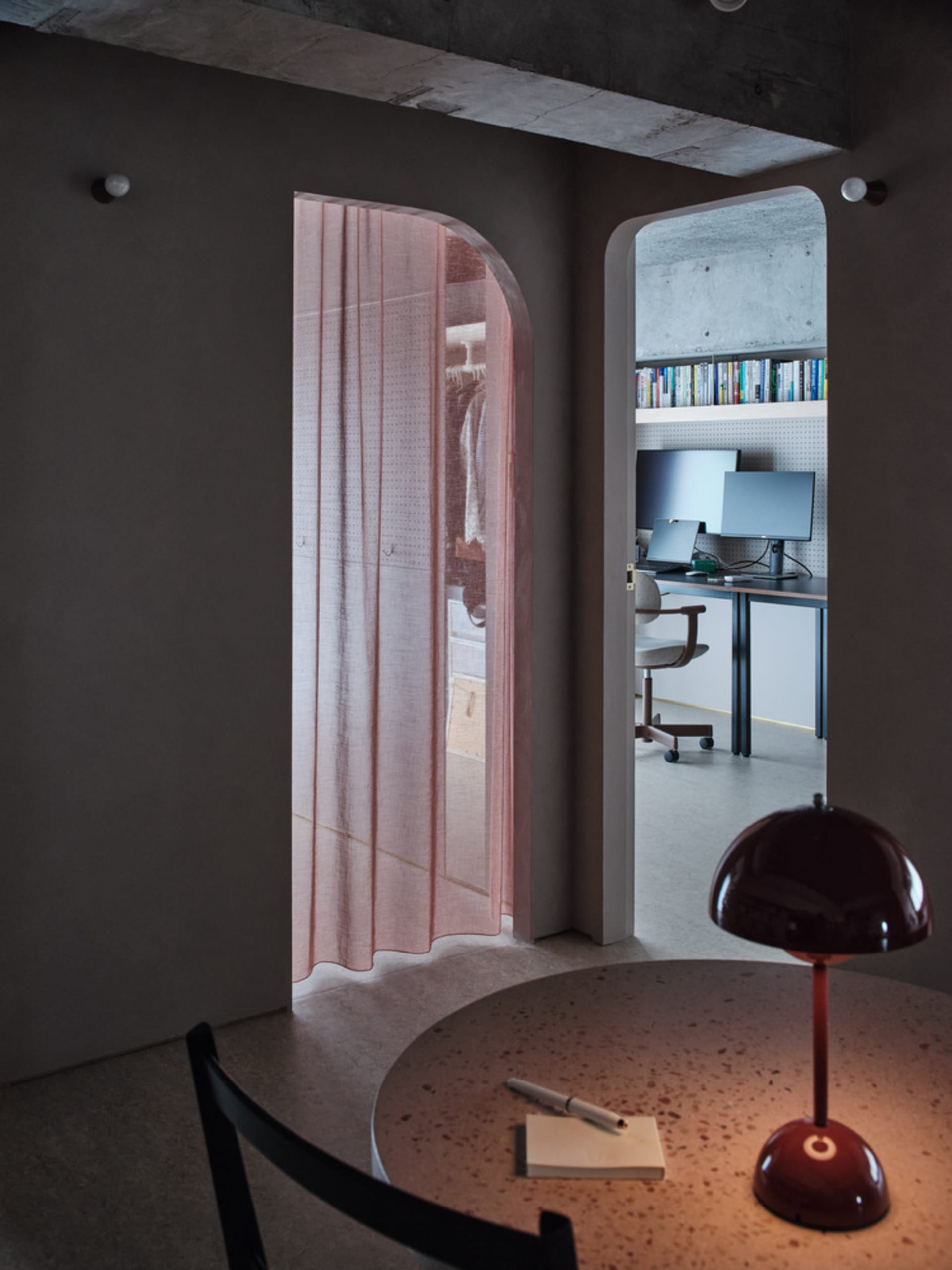 A modern home office with a pink curtain, computer desk, and bookshelf.