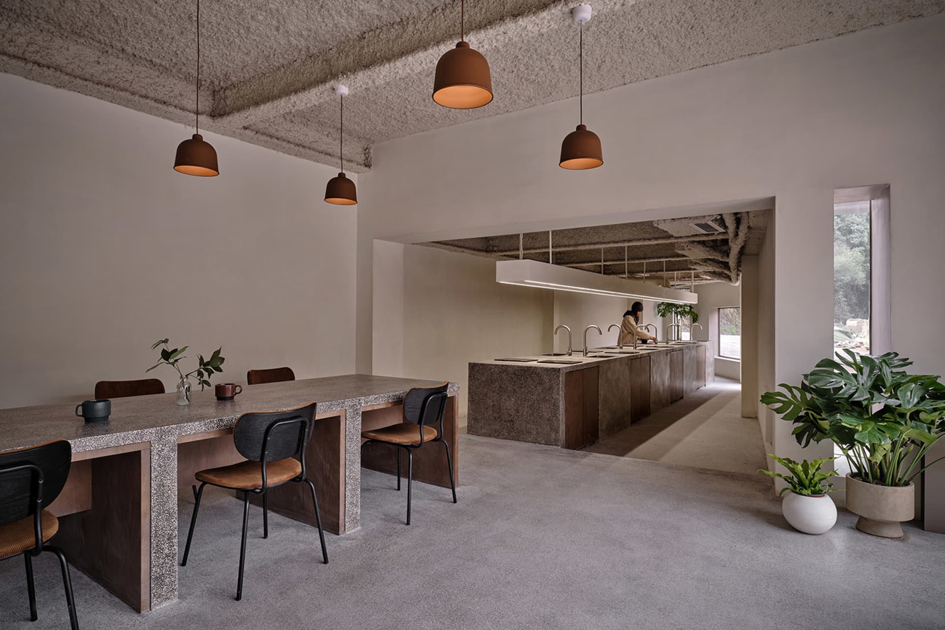 Minimalist cafe interior with concrete walls, wood furniture, and hanging pendant lights.
