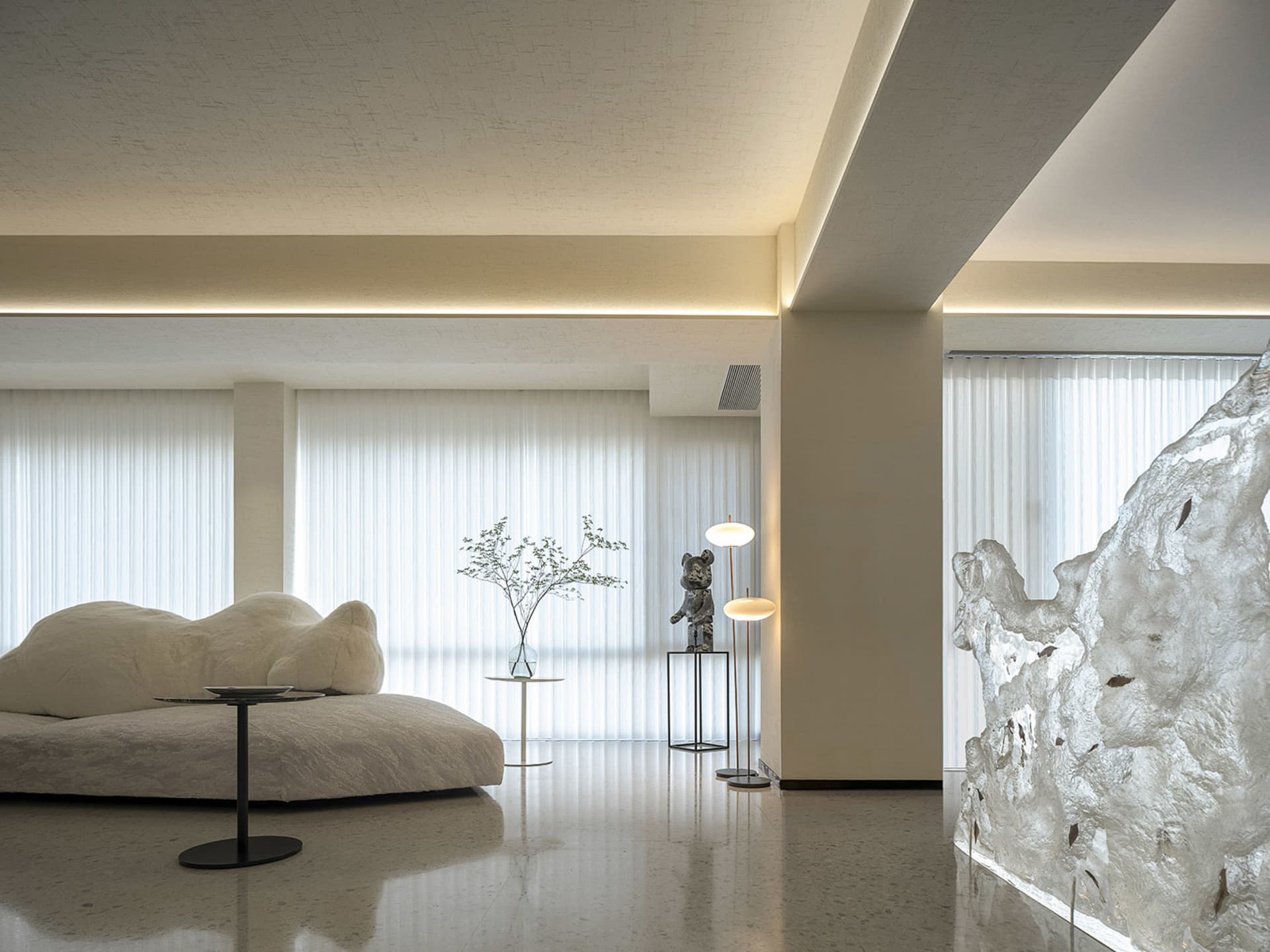 Modern minimalist living room featuring glass and metal elements and white, vertical blinds allowing natural light in.