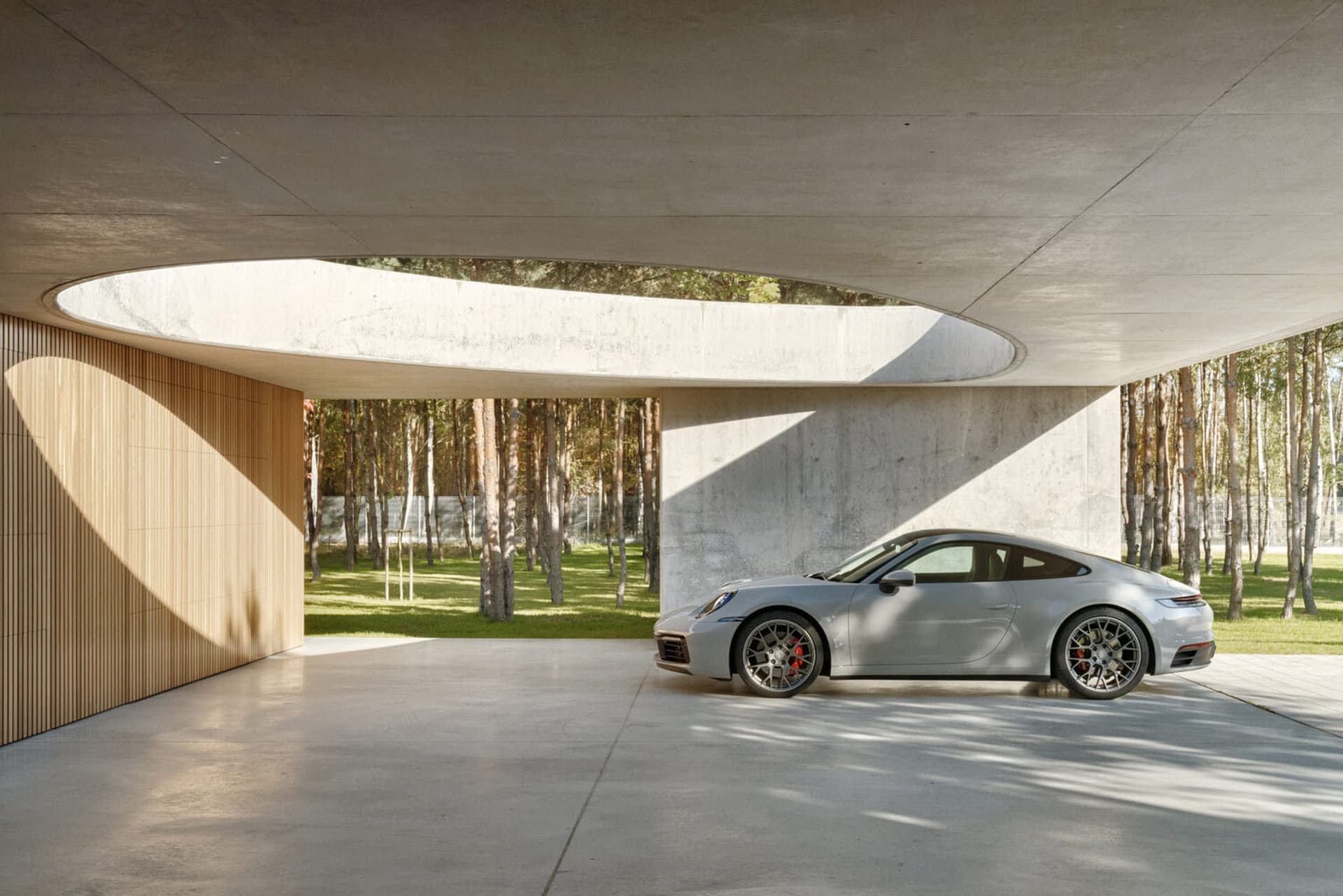 A modern architectural space featuring a gray car parked in an outdoor garage or structure with concrete walls and a large ci