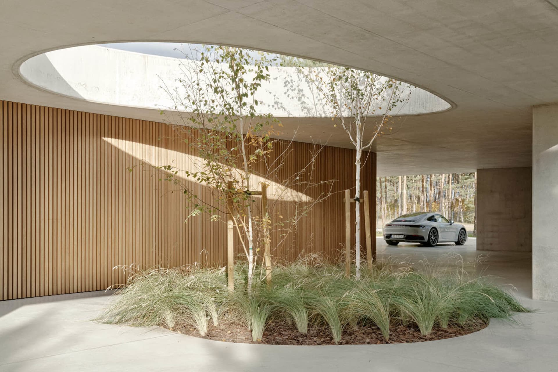 Circular wooden roof interior with plants and a Porsche 911 in the background.