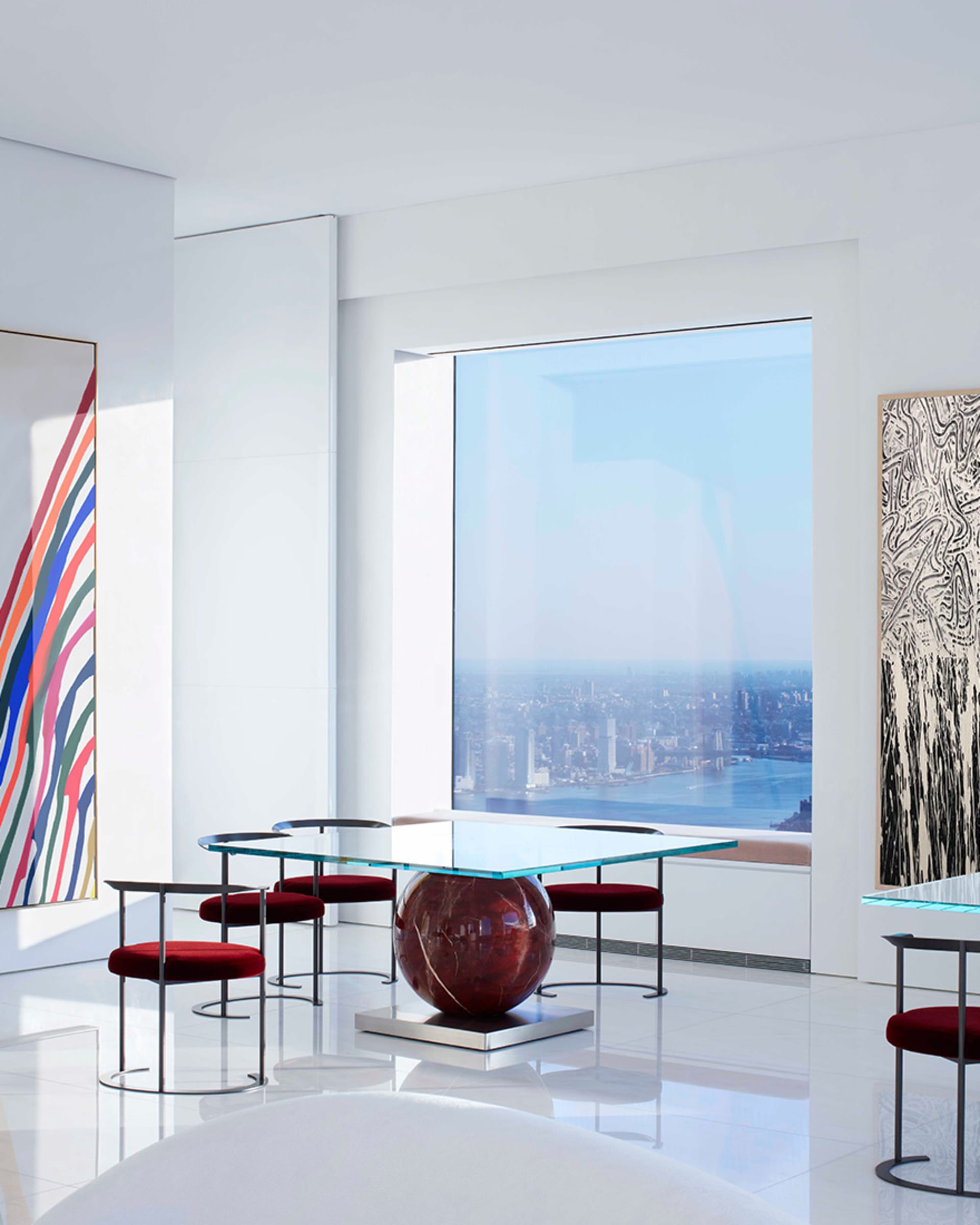 Modern living room with glass table, metal chairs, and red fabric seating.