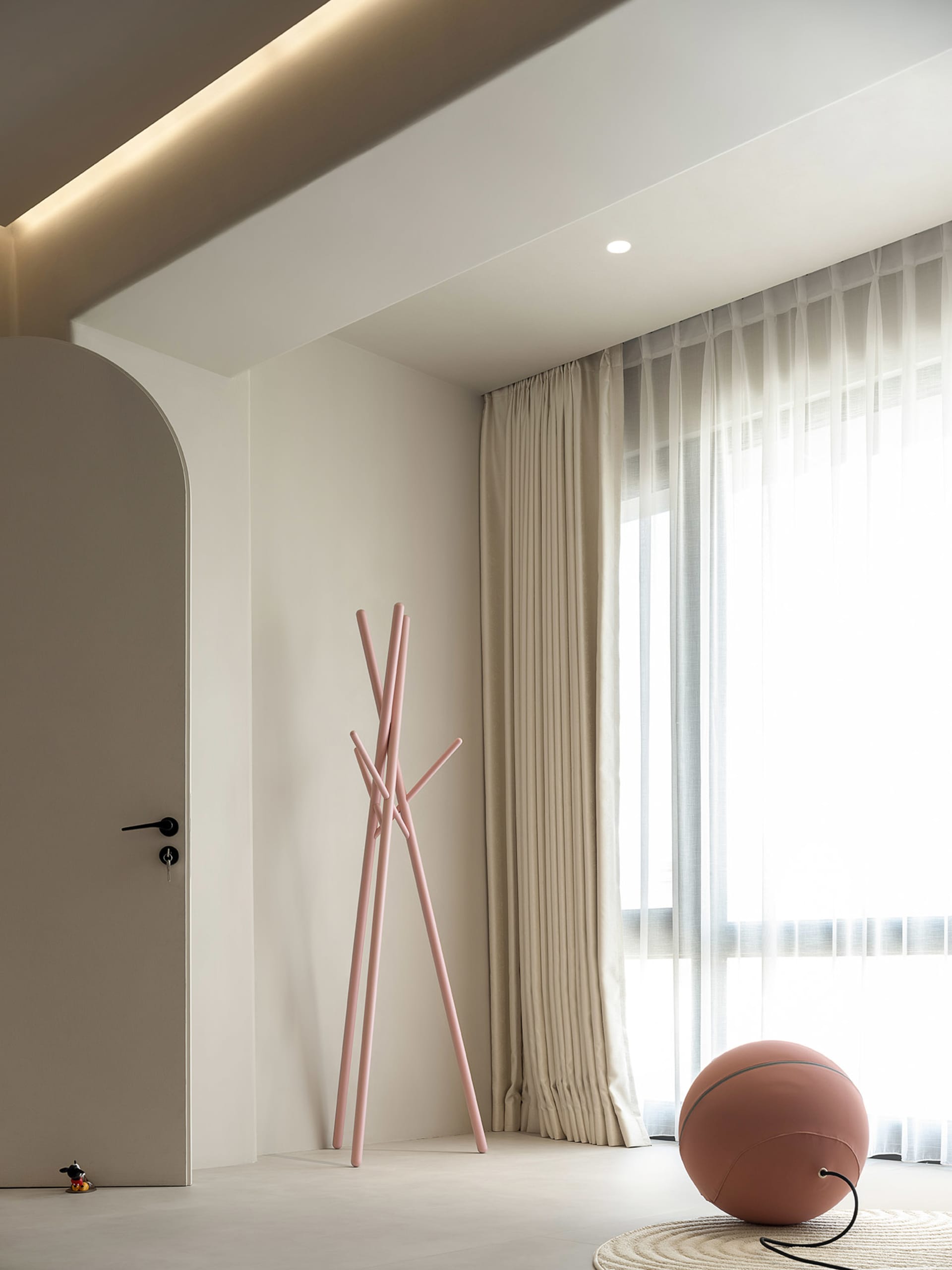 A minimalist living room with neutral colors, fabric curtains, and a metal coat rack.