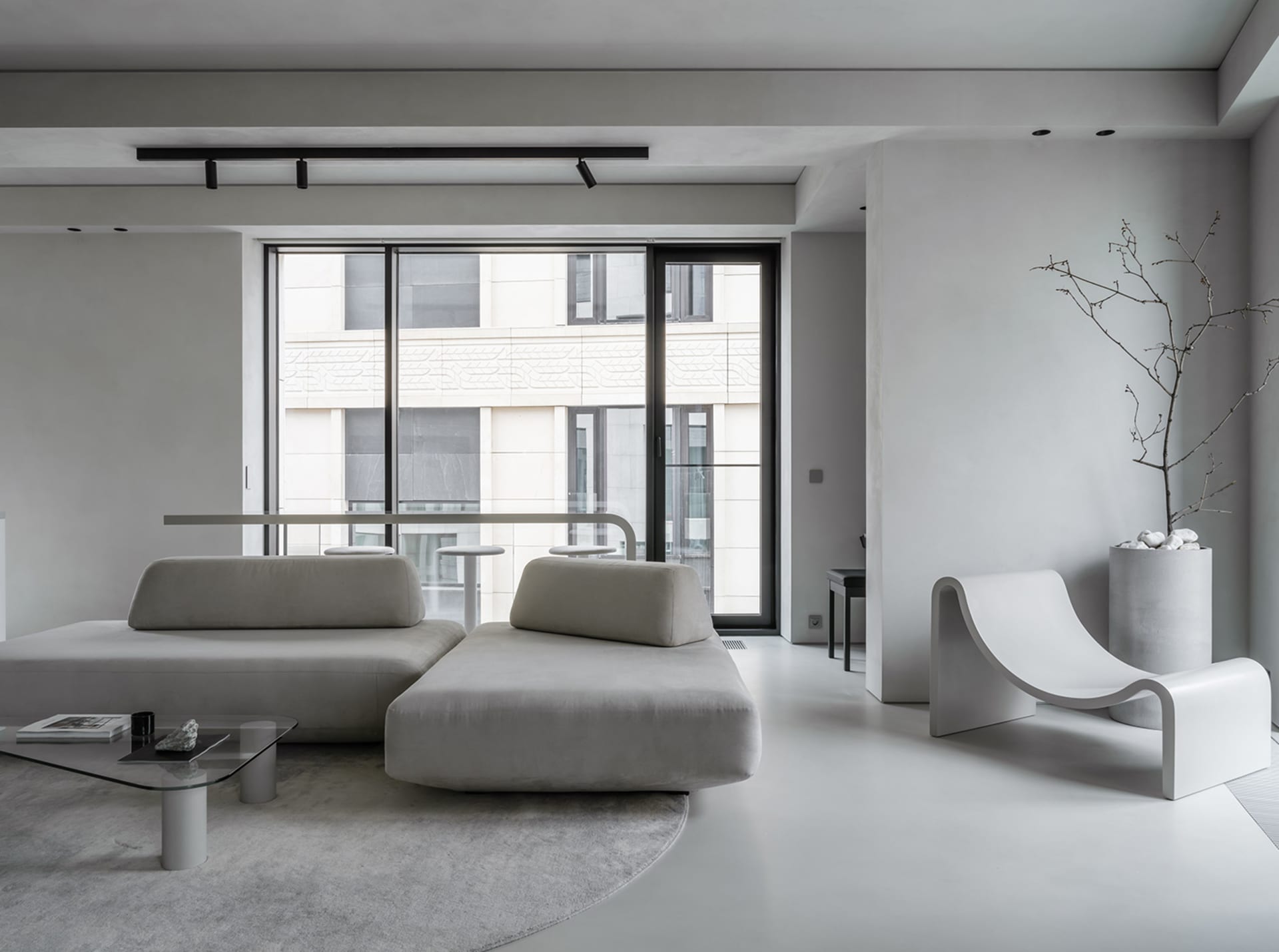 A modern minimalist living room with a concrete floor, a large window, and a sleek, curved lounge chair.