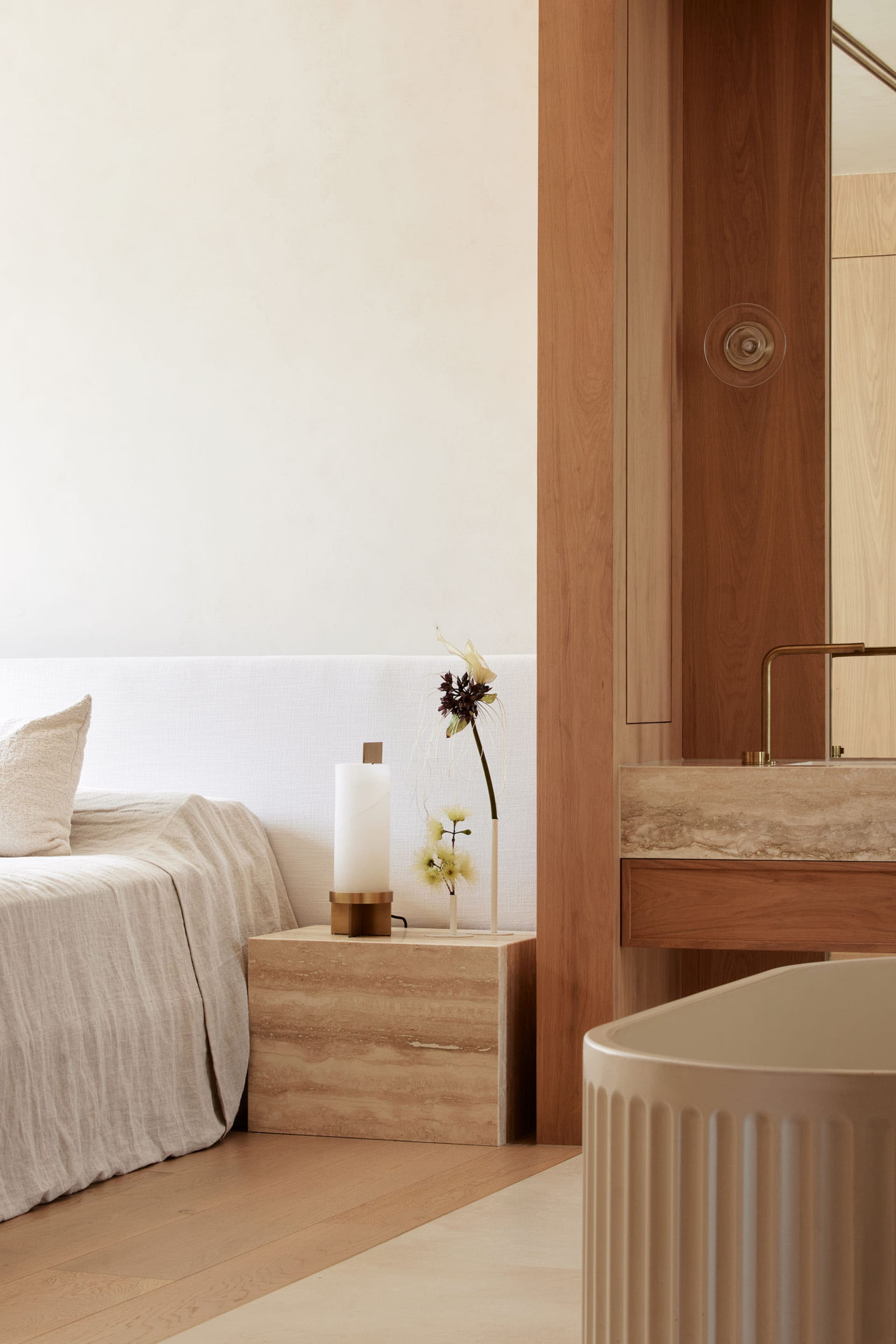 A minimalist bedroom with white walls, a white bed, a marble nightstand, and a vase with flowers.