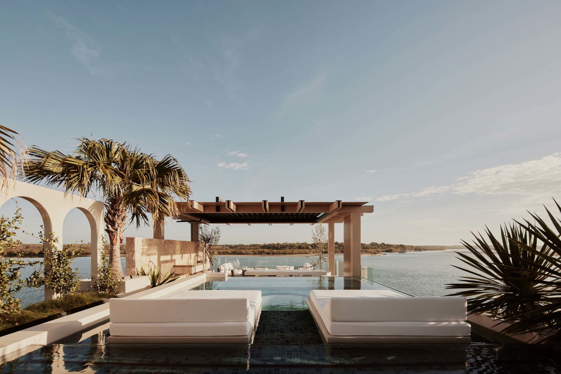 A serene residential area featuring an infinity pool with glass surroundings and a stone patio.