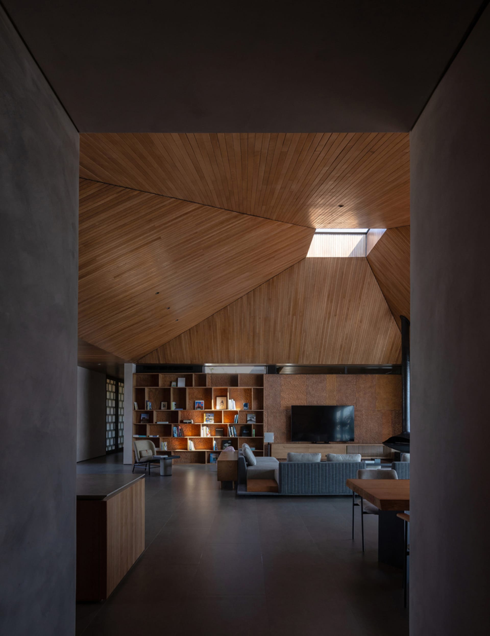 A modern living room with a wooden ceiling, a bookshelf, and a sofa.