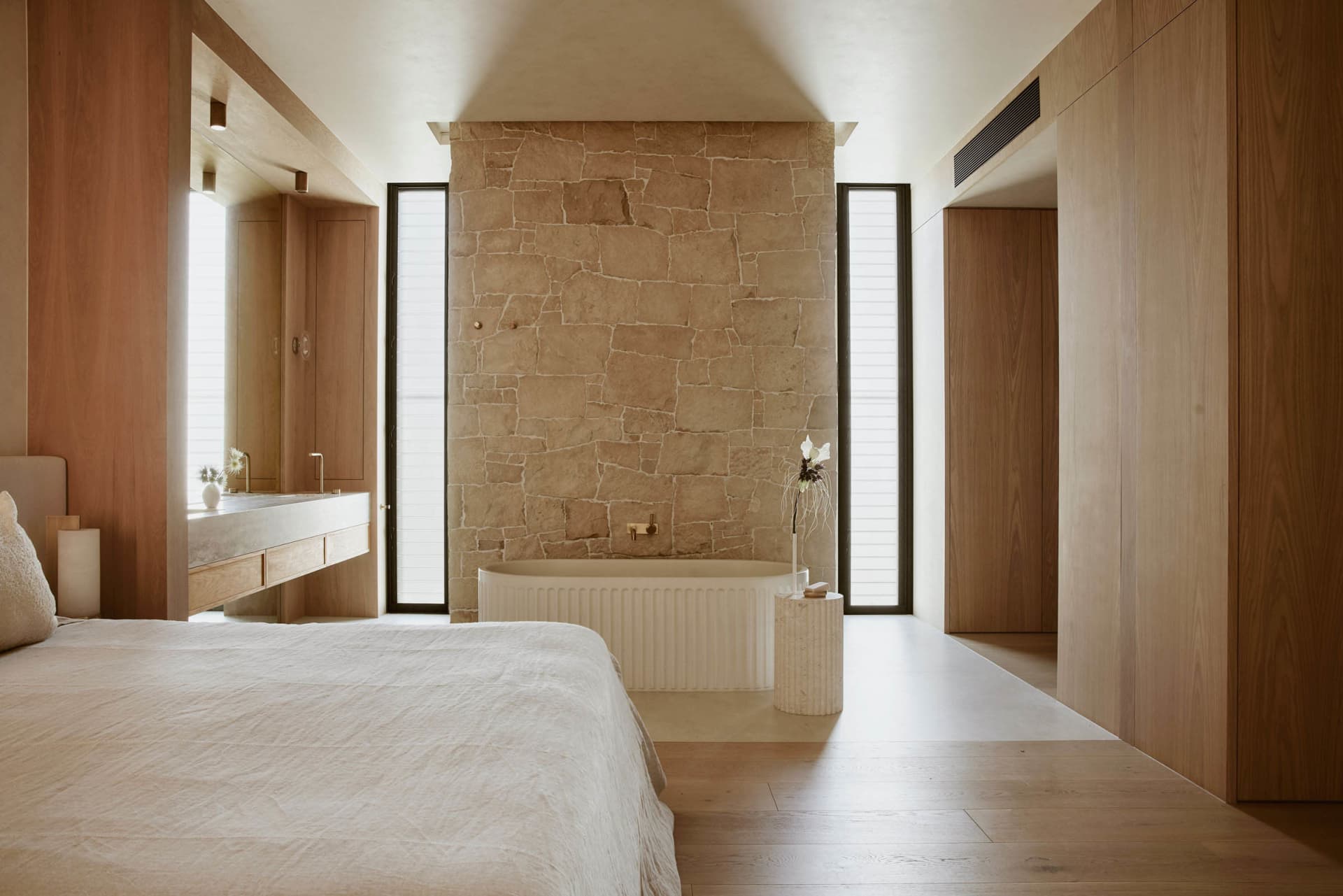 A minimalist bedroom with a large bed, a wooden floor, and a white plaster wall in the center.