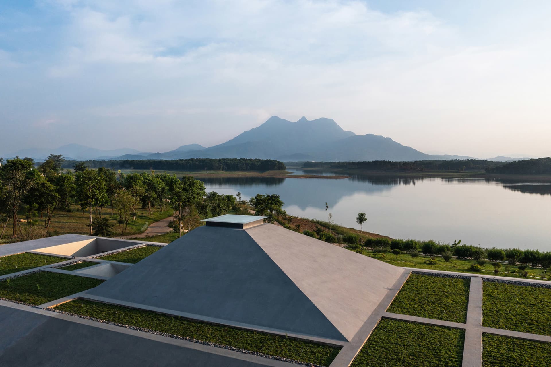 一座極簡混凝土亭閣俯瞰寧靜湖面，背景為山巒。
