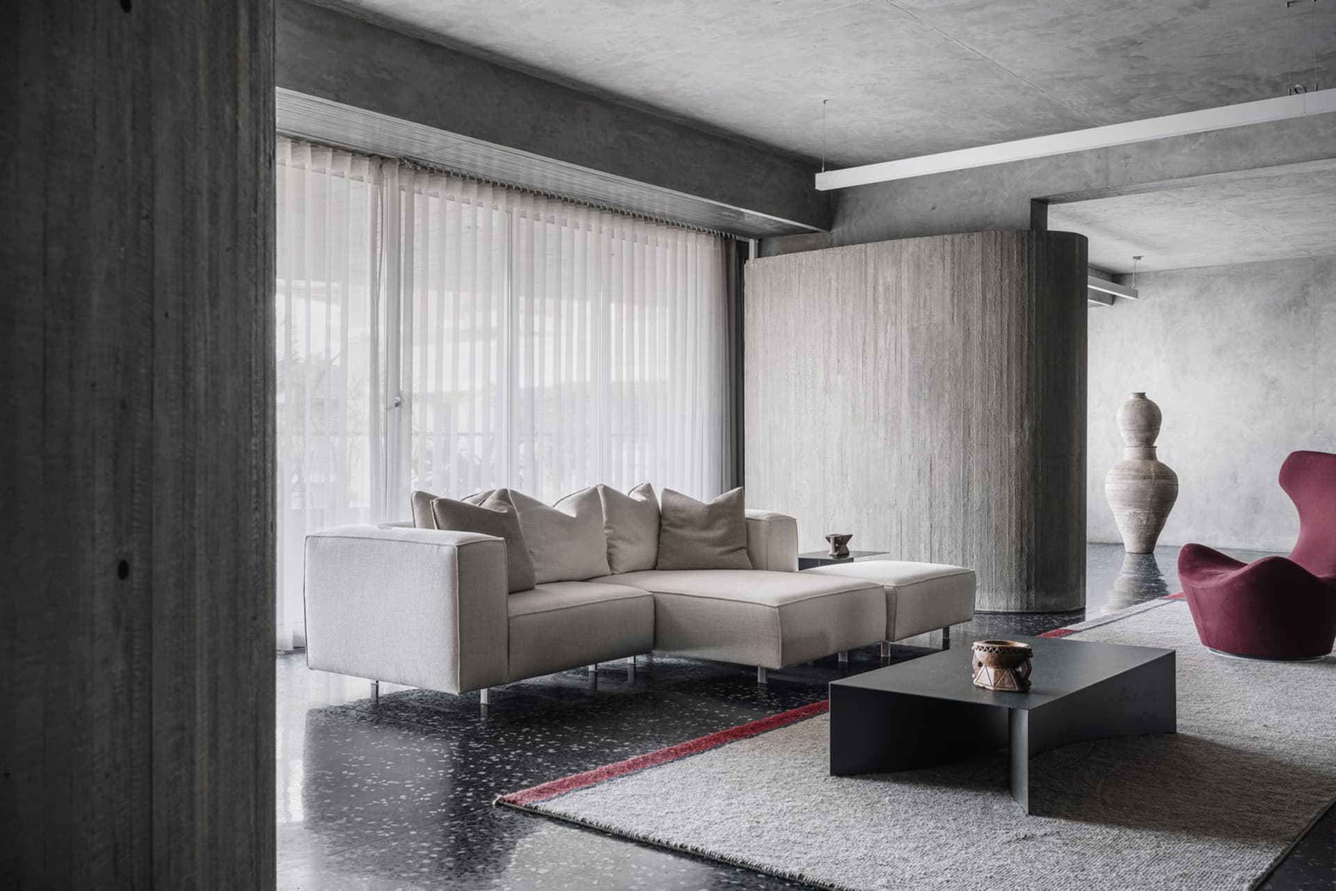A modern living room with concrete walls, a fabric sofa, and glass windows.
