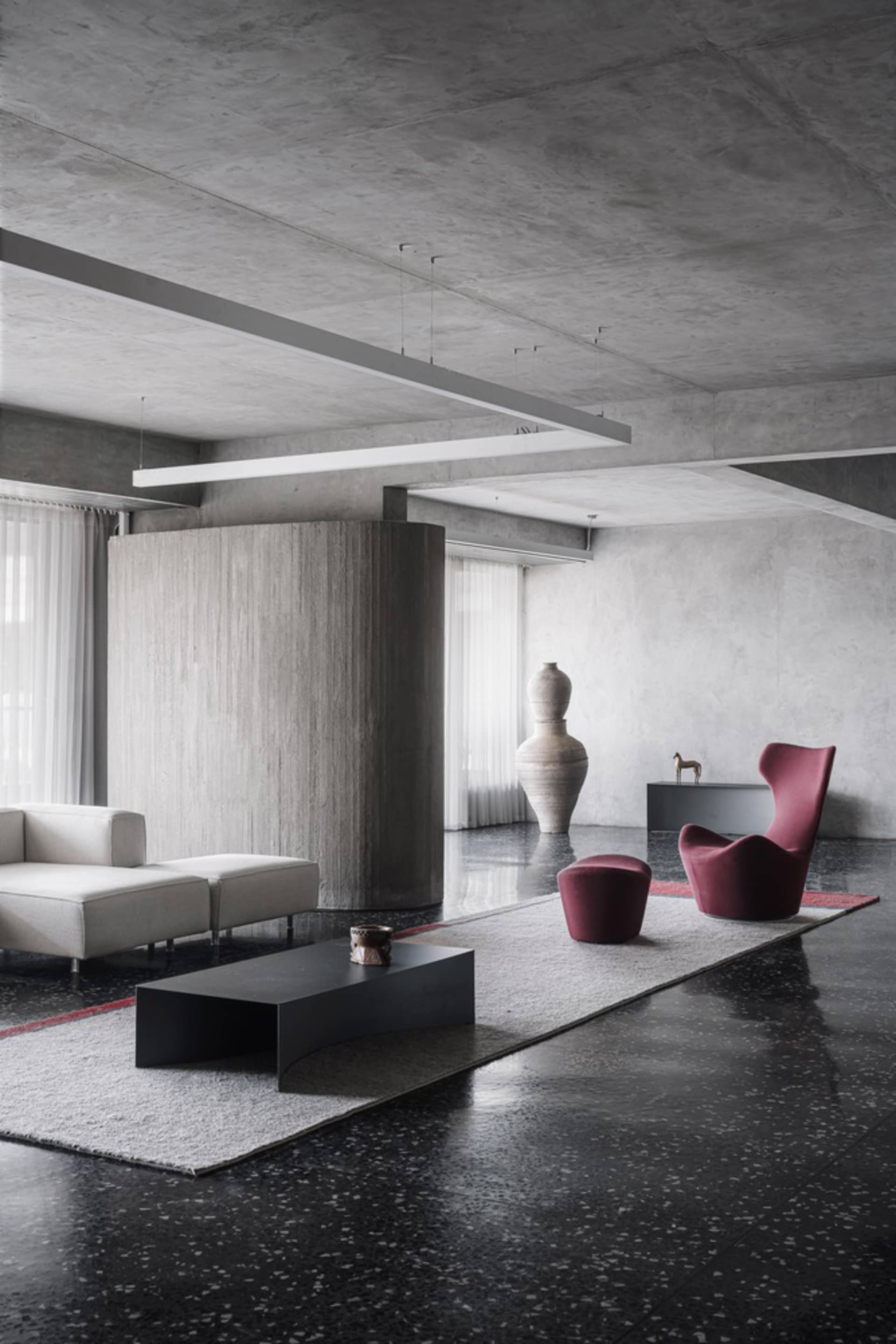 A modern minimalist living room with concrete walls, a terrazzo floor, and leather furniture and accents.
