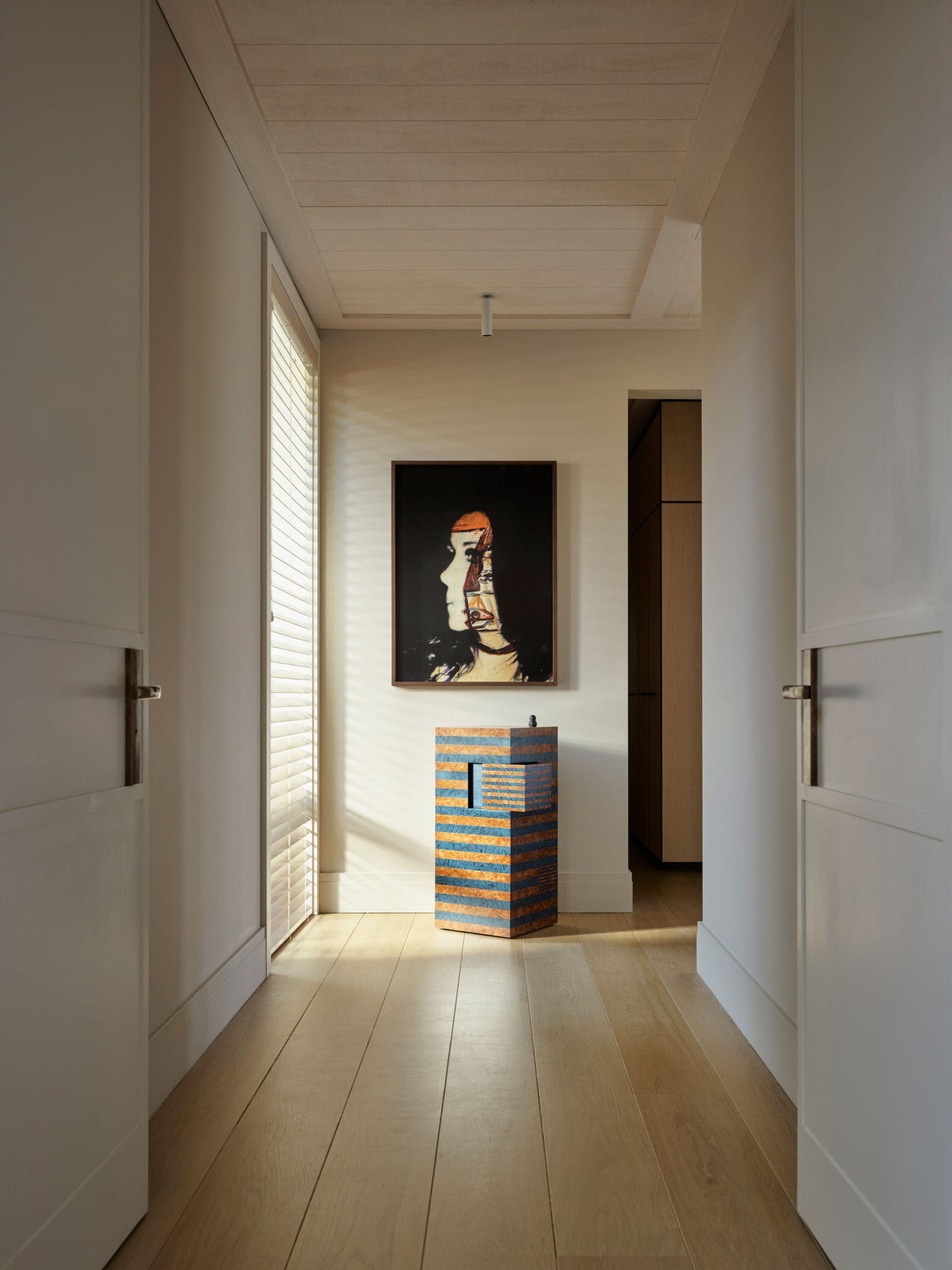 A modern, minimalist corridor interior featuring neutral-toned walls and a wooden floor with doors on either side.