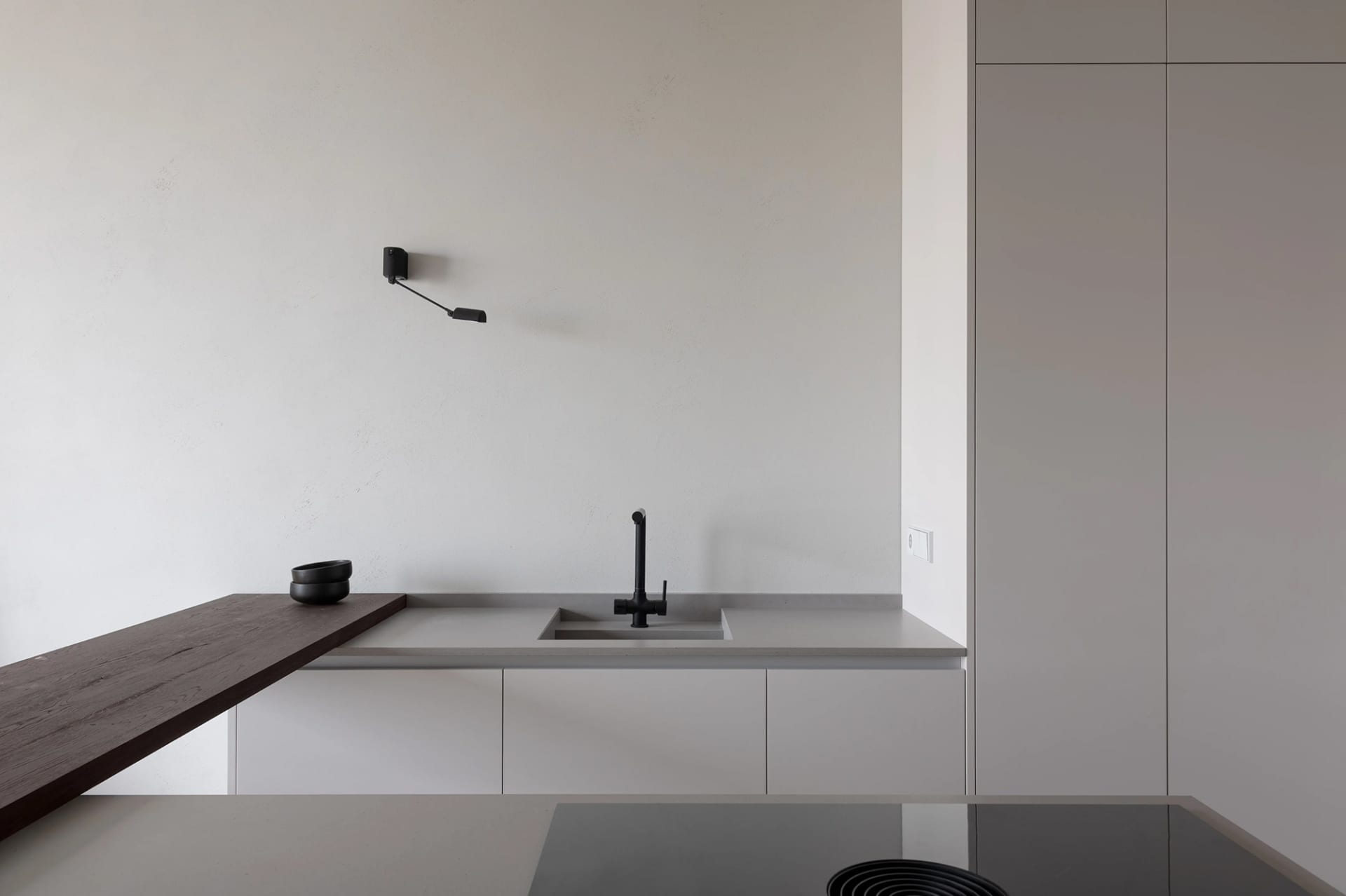 A minimalist modern kitchen featuring concrete countertops, stone backsplash, and a mixer sink.