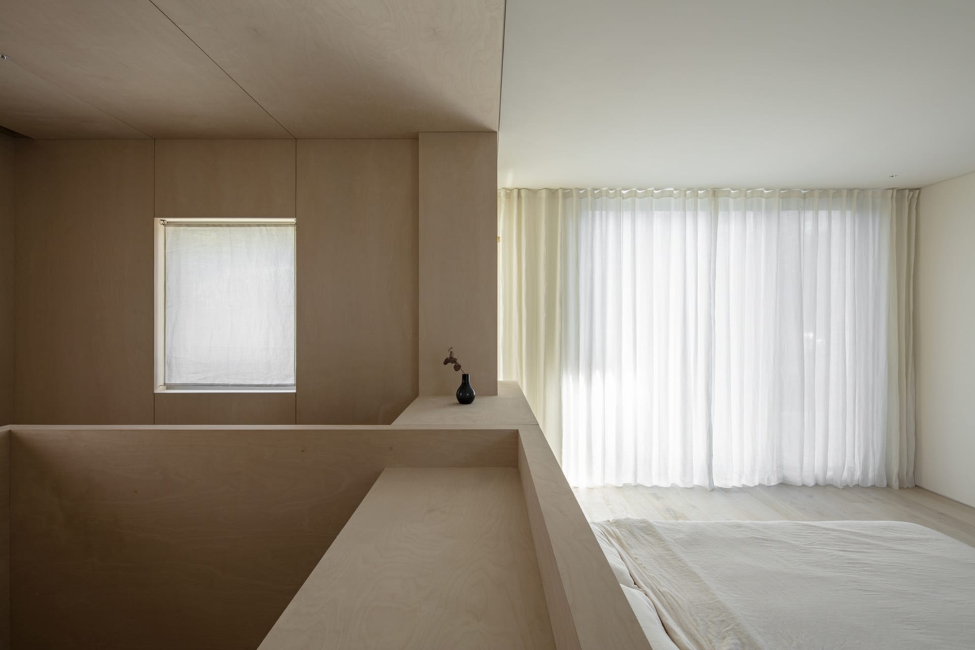 A minimalist bedroom with wooden walls, fabric curtains, and a simple bed setup.