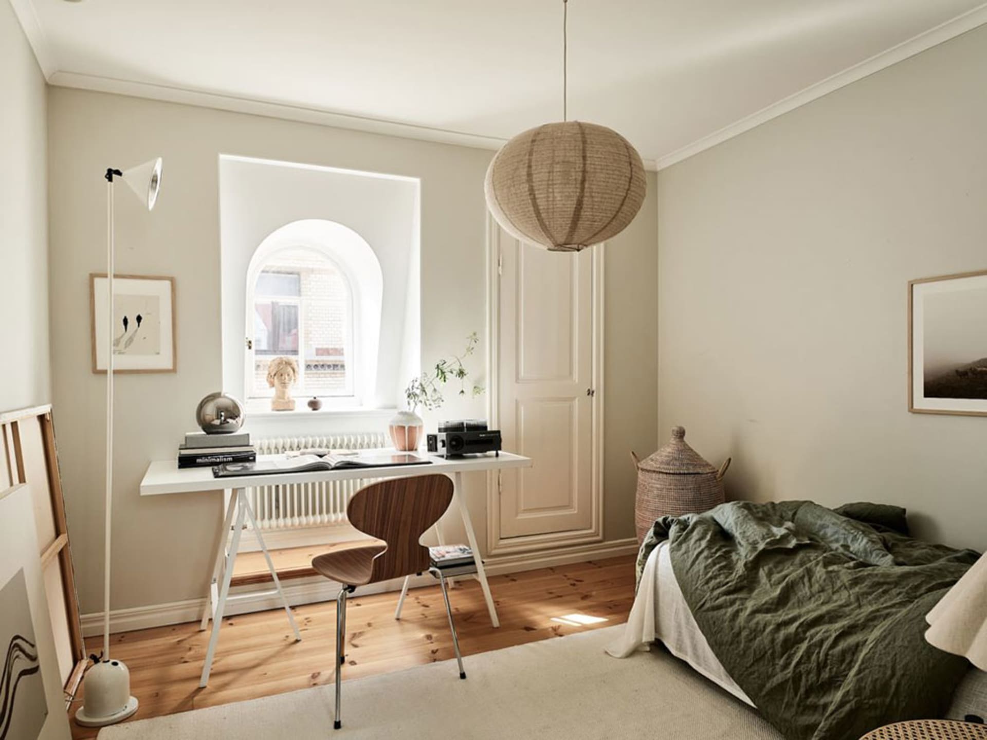 A minimalist residential bedroom featuring a wooden desk, a large window, and a comfortable bed.