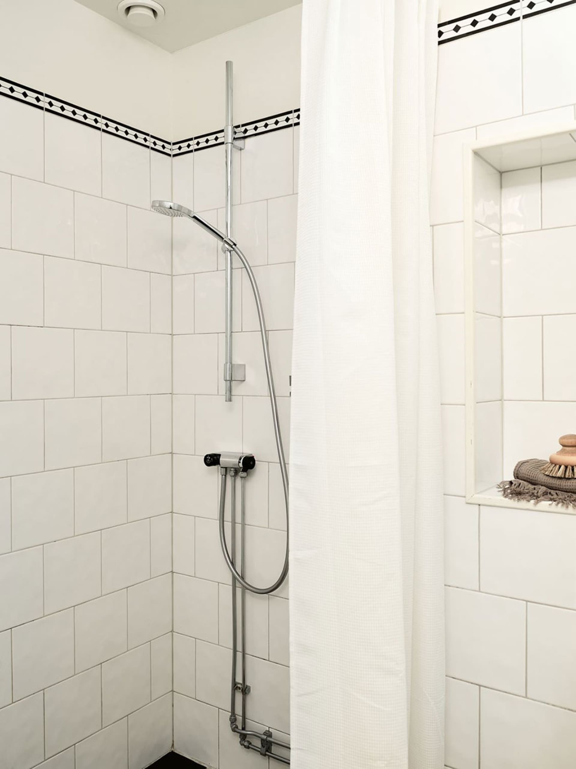 White-tiled minimalist bathroom shower area with a shower curtain and built-in niche.
